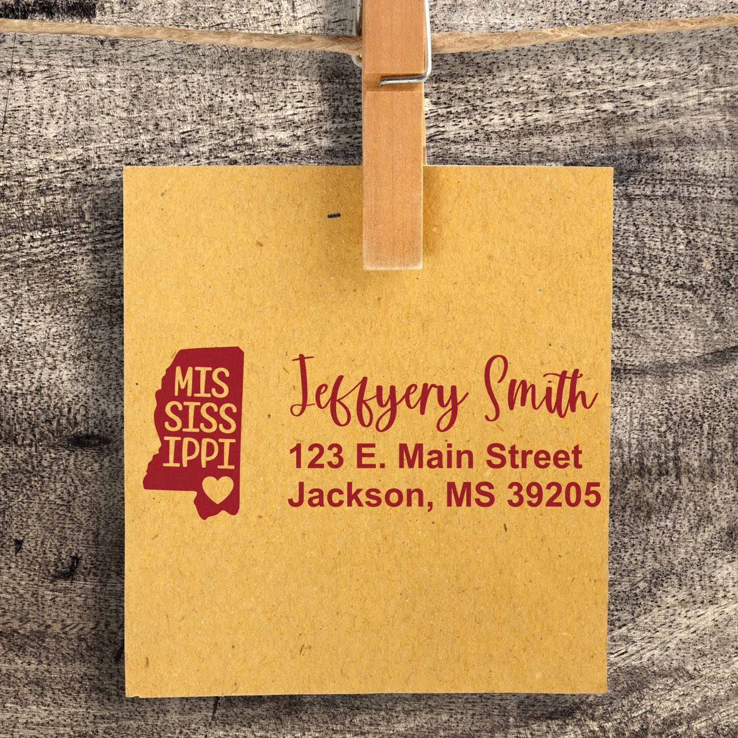 Slim Mississippi Custom Address Stamp for Envelopes displayed on a brown card with a clothespin, featuring a state outline and personalized address in red text.