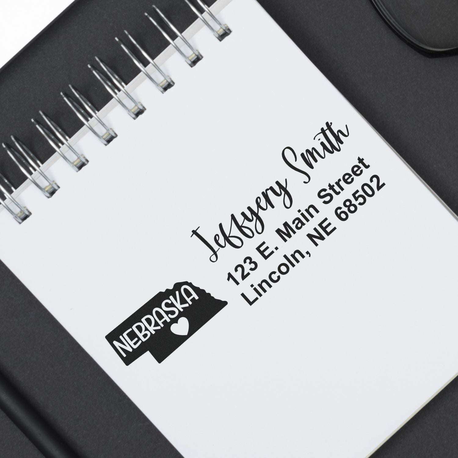 State Love of Nebraska Custom Address Stamp Self-Inking displayed on a notepad, featuring a Nebraska state outline with a heart and personalized address details in black ink.