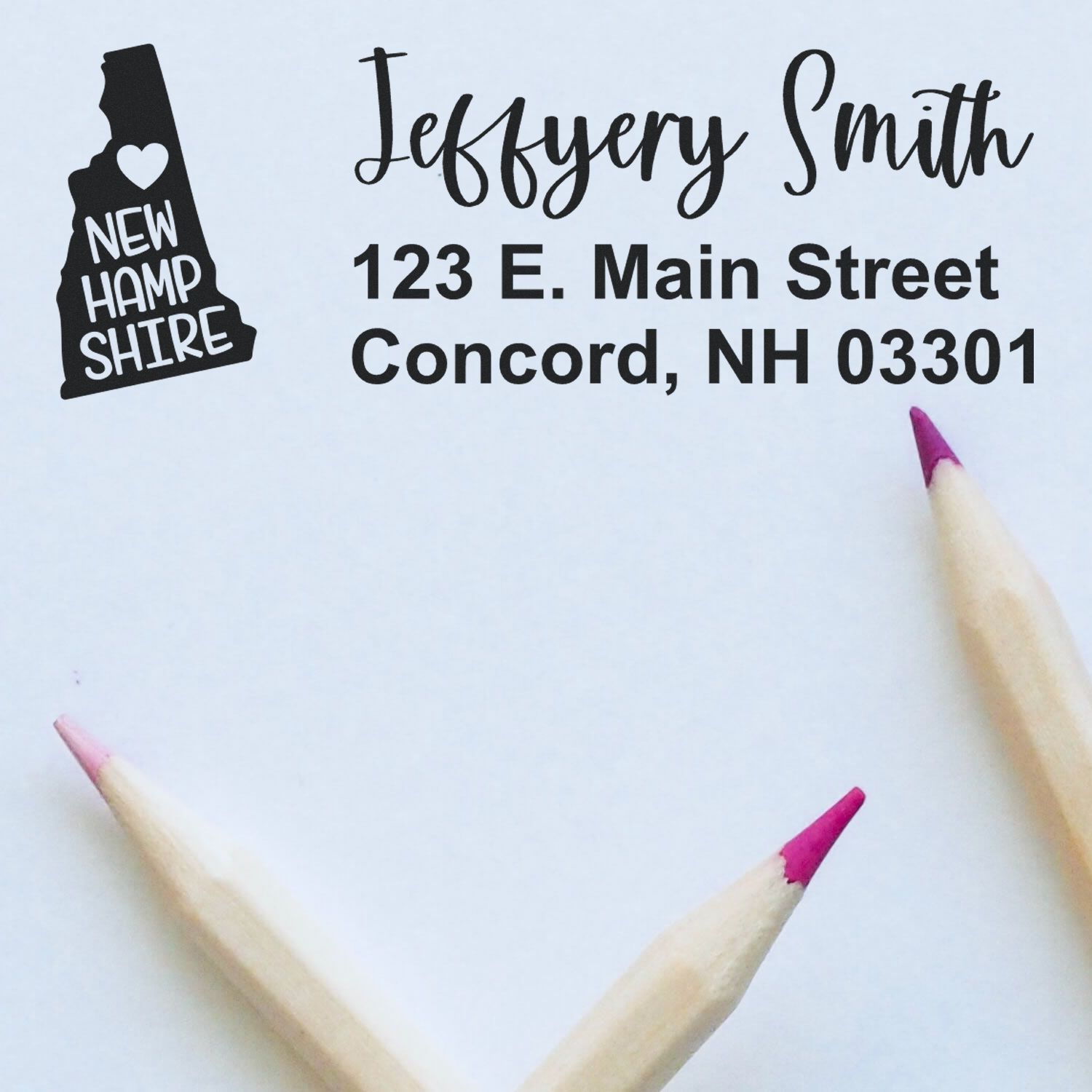 New Hampshire State Love Personalized Address Stamp on white paper with pink-tipped pencils. Features state silhouette and custom address: Jeffery Smith, 123 E. Main Street, Concord, NH 03301.