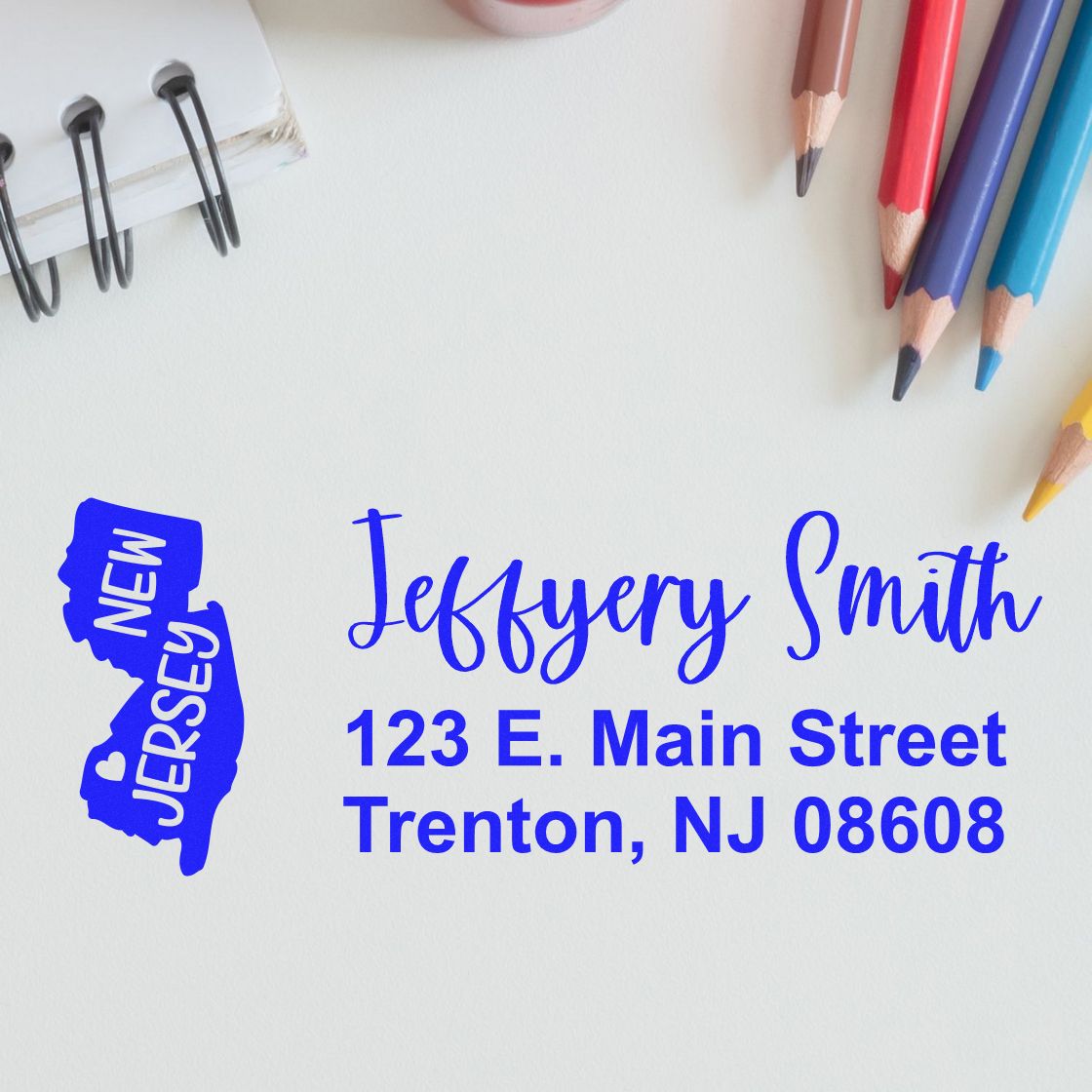 New Jersey State Love Personalized Address Stamp on paper with colorful pencils and a notebook. The stamp features a blue outline of New Jersey and custom address text in a stylish font.