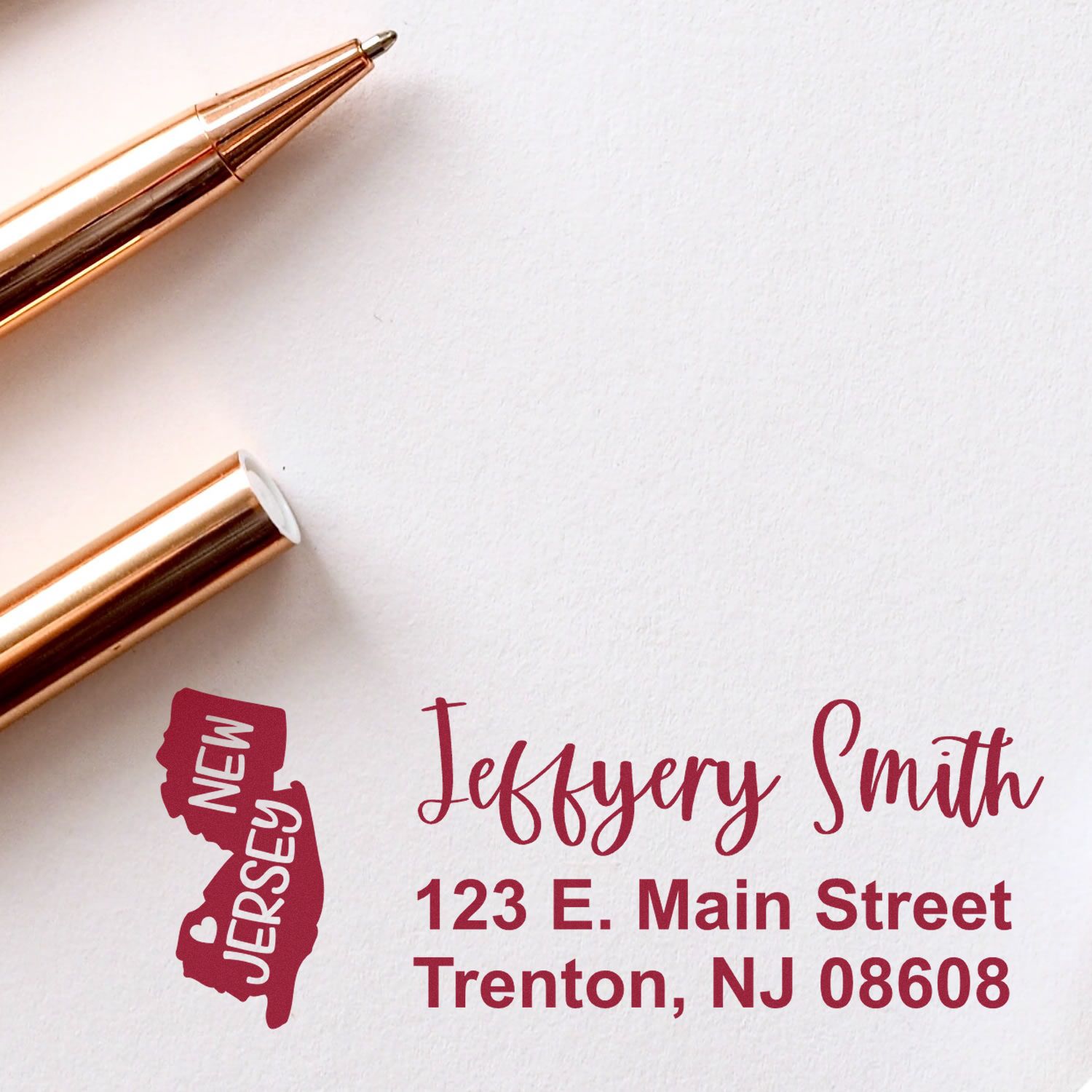 New Jersey State Love Personalized Address Stamp on white paper with a rose gold pen. The stamp features a New Jersey map design and custom address in red ink.