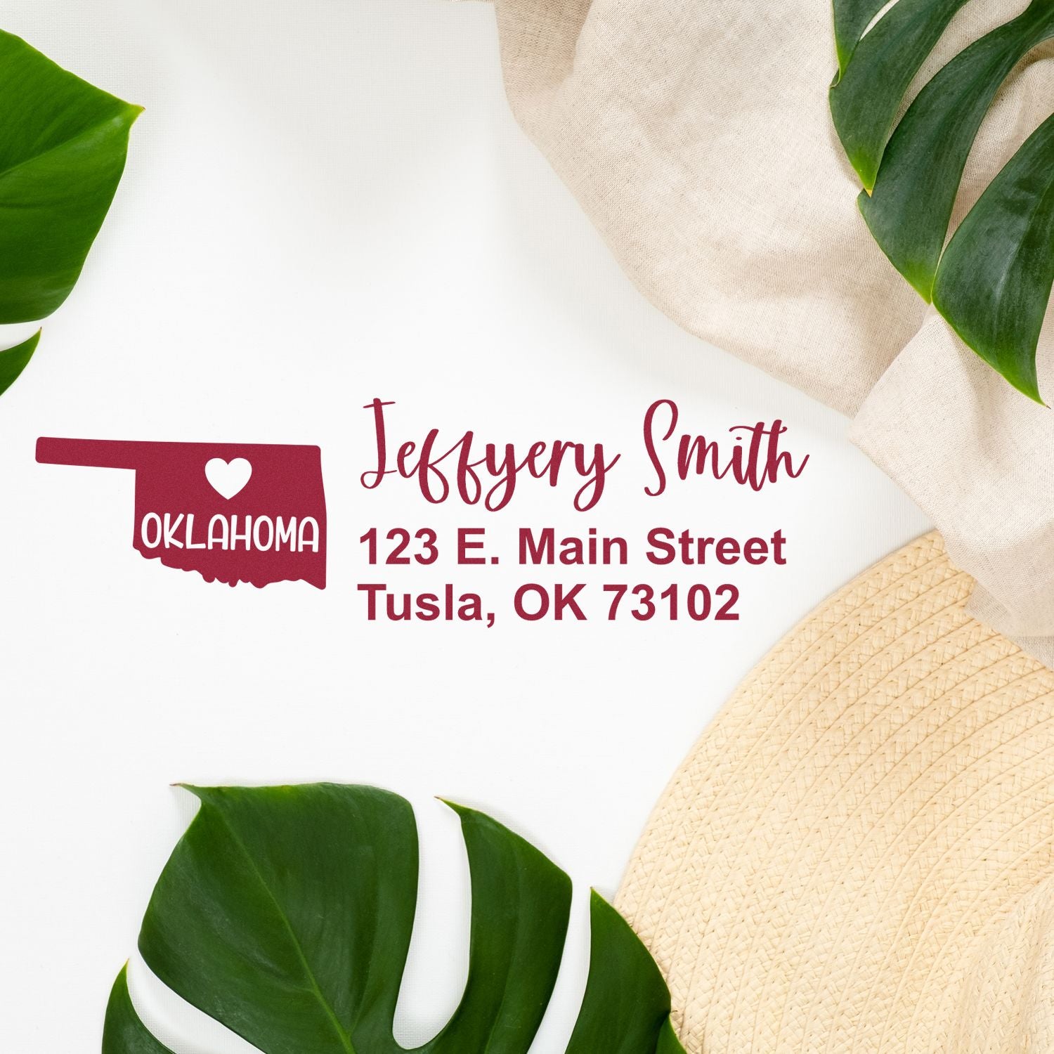 PSI Pre-Inked Oklahoma State Love Customized Address Stamp on white surface with green leaves and beige fabric. Displays name and address in red with Oklahoma state outline and heart design.