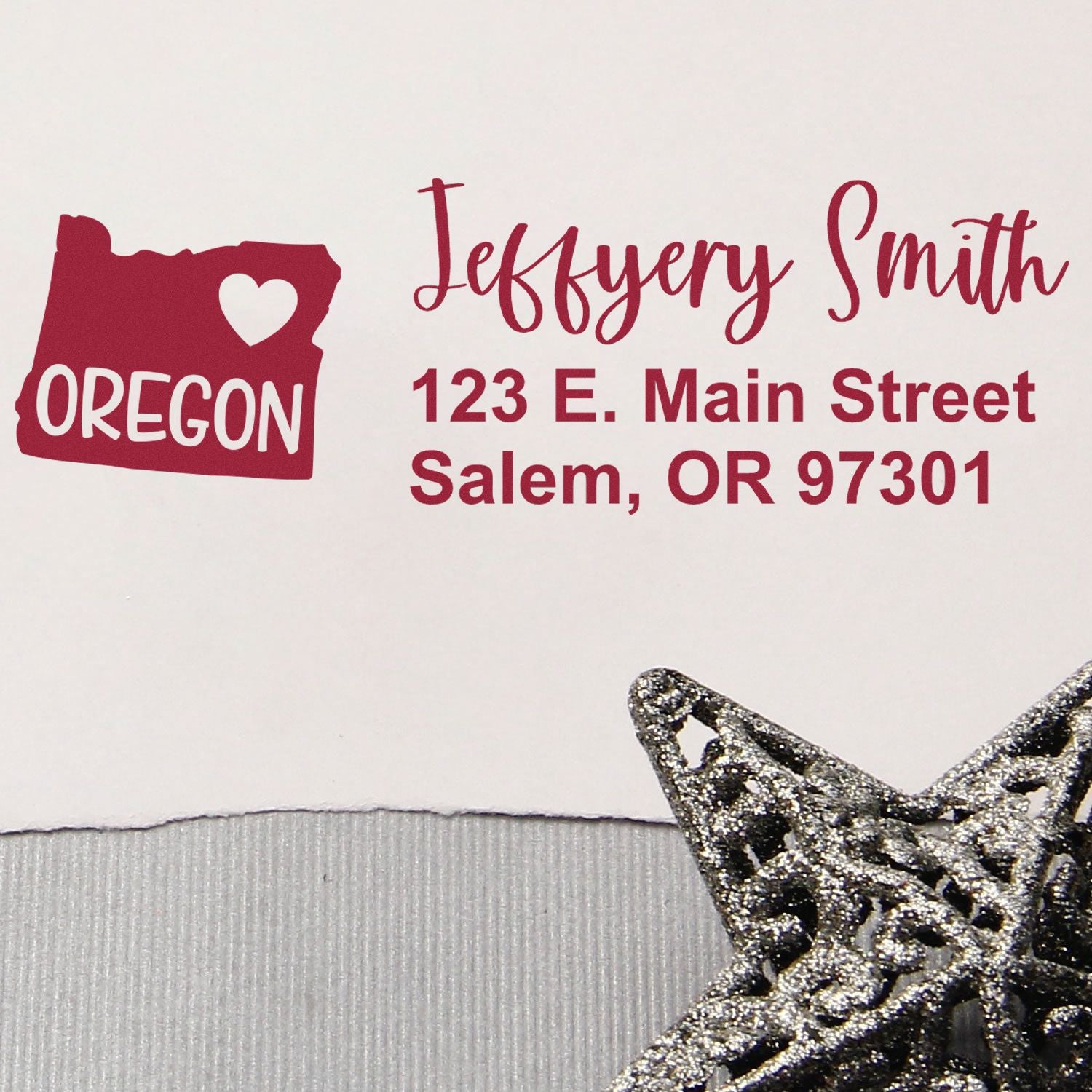 Slim Oregon Custom Address Stamp for Envelopes displayed on a white envelope with a red Oregon state design and address text. A decorative silver star is placed nearby.