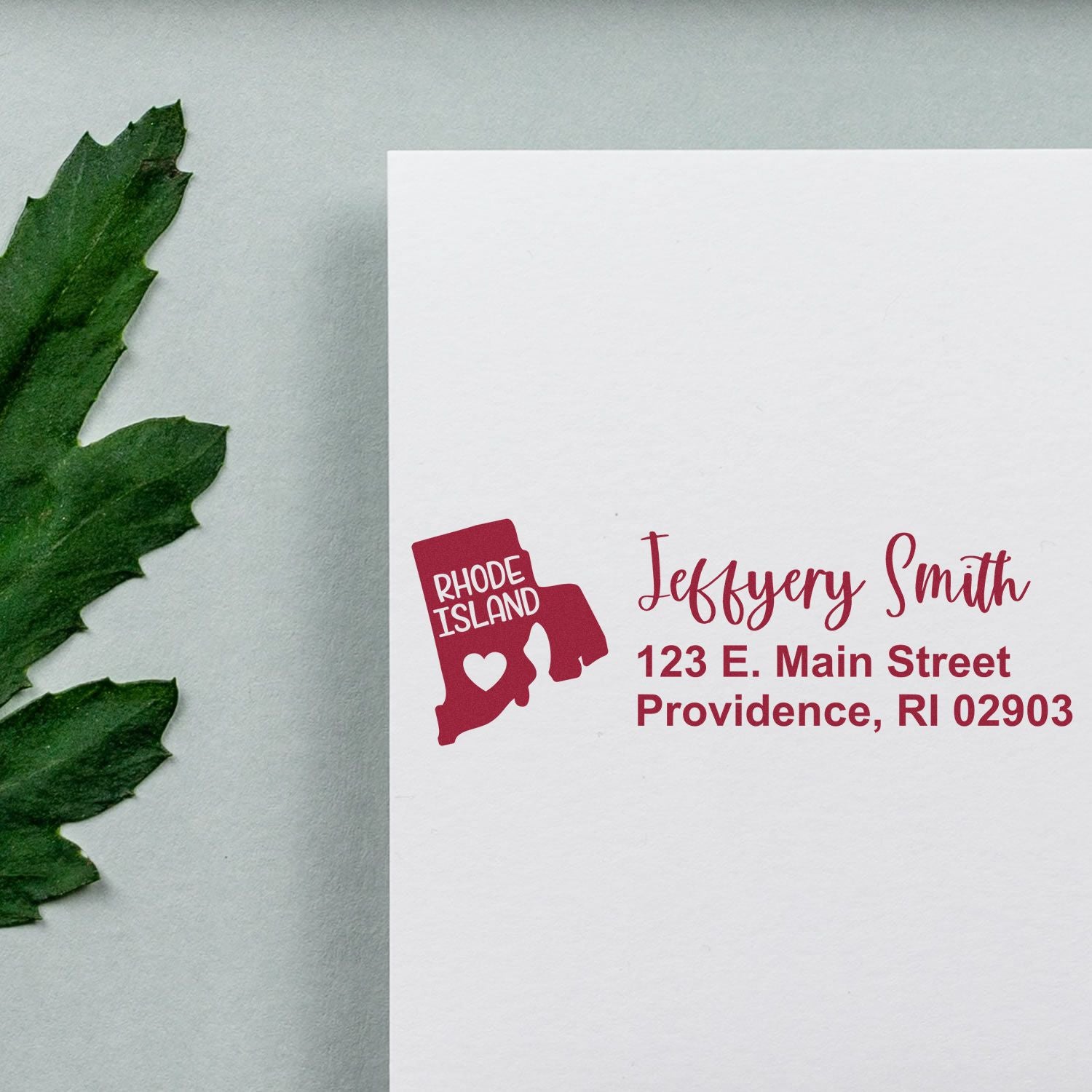 PSI Pre-Inked Rhode Island State Love Customized Address Stamp on white envelope with red ink, featuring a Rhode Island map design and personalized address. Green leaf decorates the background.