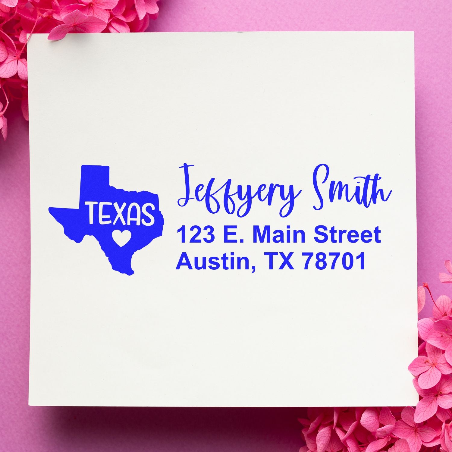 Slim Texas Custom Address Stamp for Envelopes displayed on a white card with blue text, featuring a Texas map design. The card is set against a pink background with pink flowers.