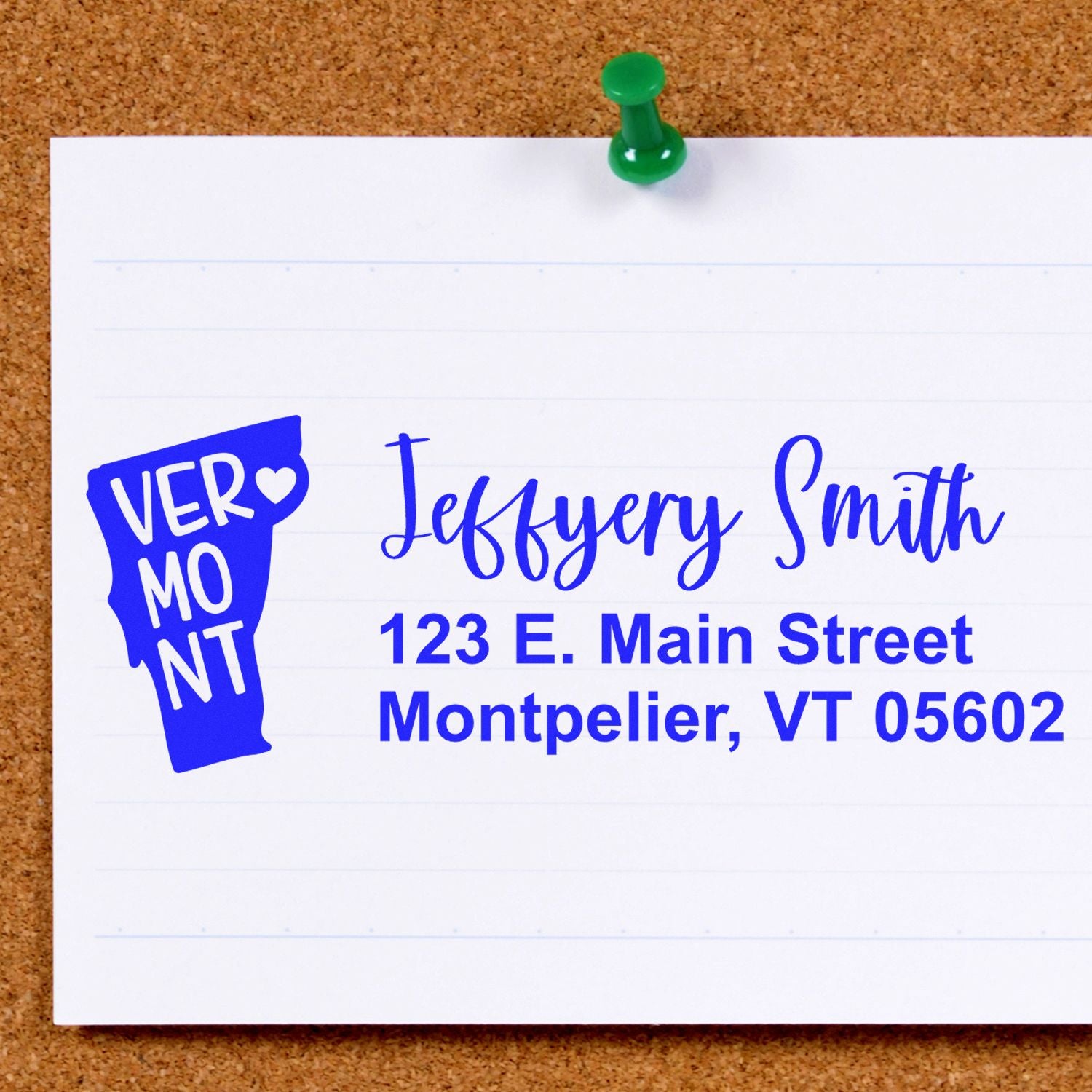 Vermont State Love Personalized Address Stamp on a corkboard. Blue ink displays Jeffery Smith, 123 E. Main Street, Montpelier, VT 05602 with a Vermont state outline and heart design.