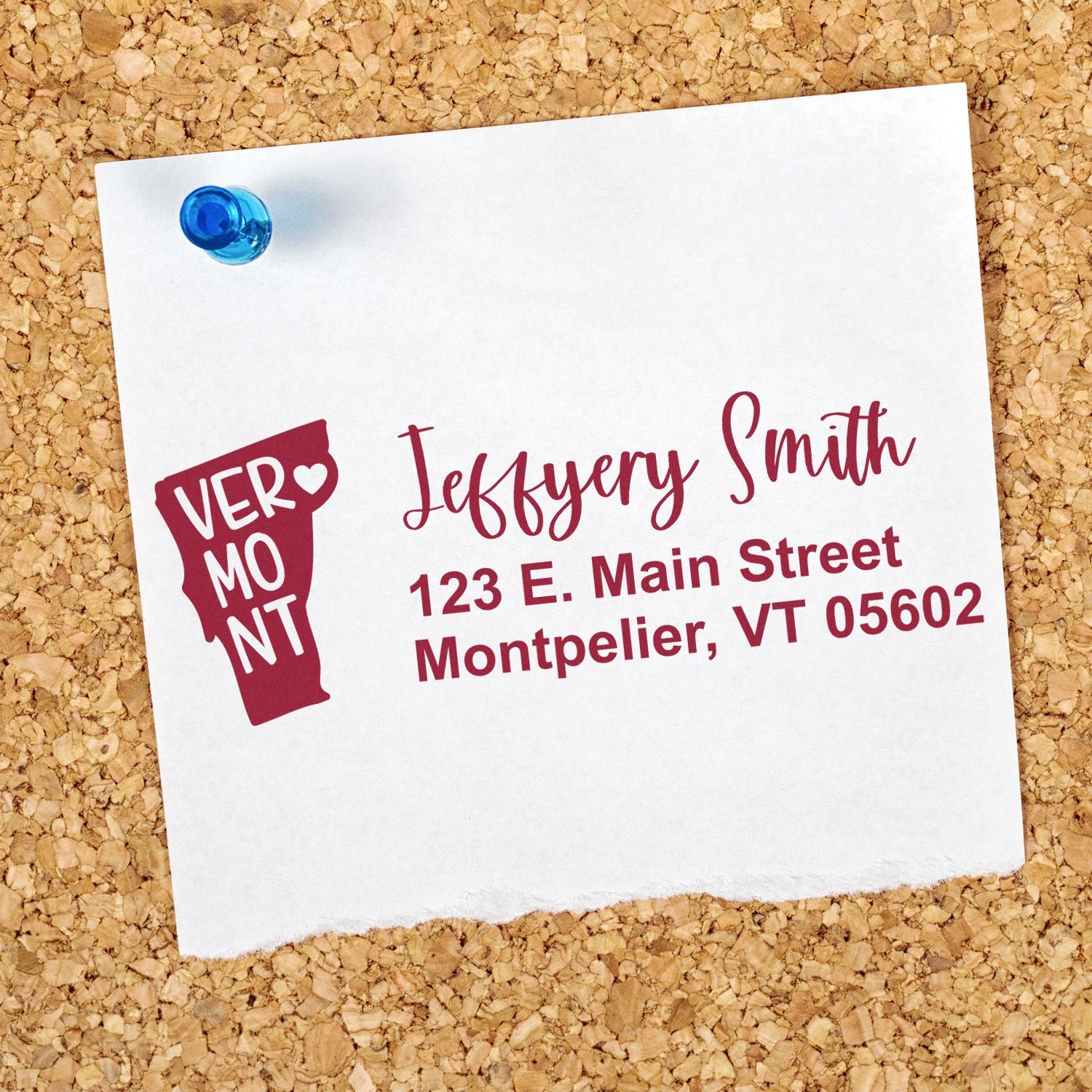 Slim Vermont Custom Address Stamp for Envelopes displayed on a corkboard. The stamp shows a name and address in elegant font with a Vermont state outline.