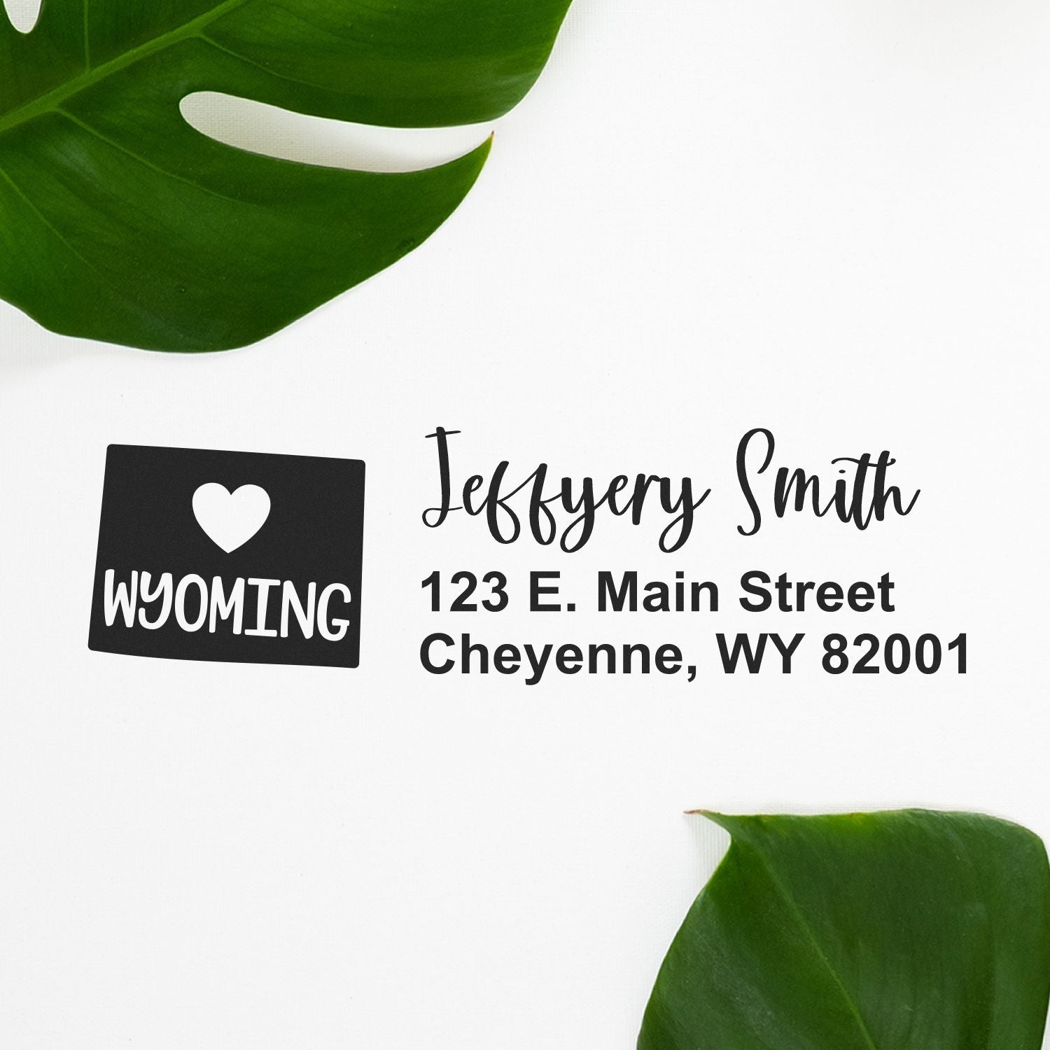 Wyoming State Love Personalized Address Stamp featuring a heart and Wyoming design, shown with the name Jeffery Smith and address in Cheyenne, WY, on a white background with green leaves.