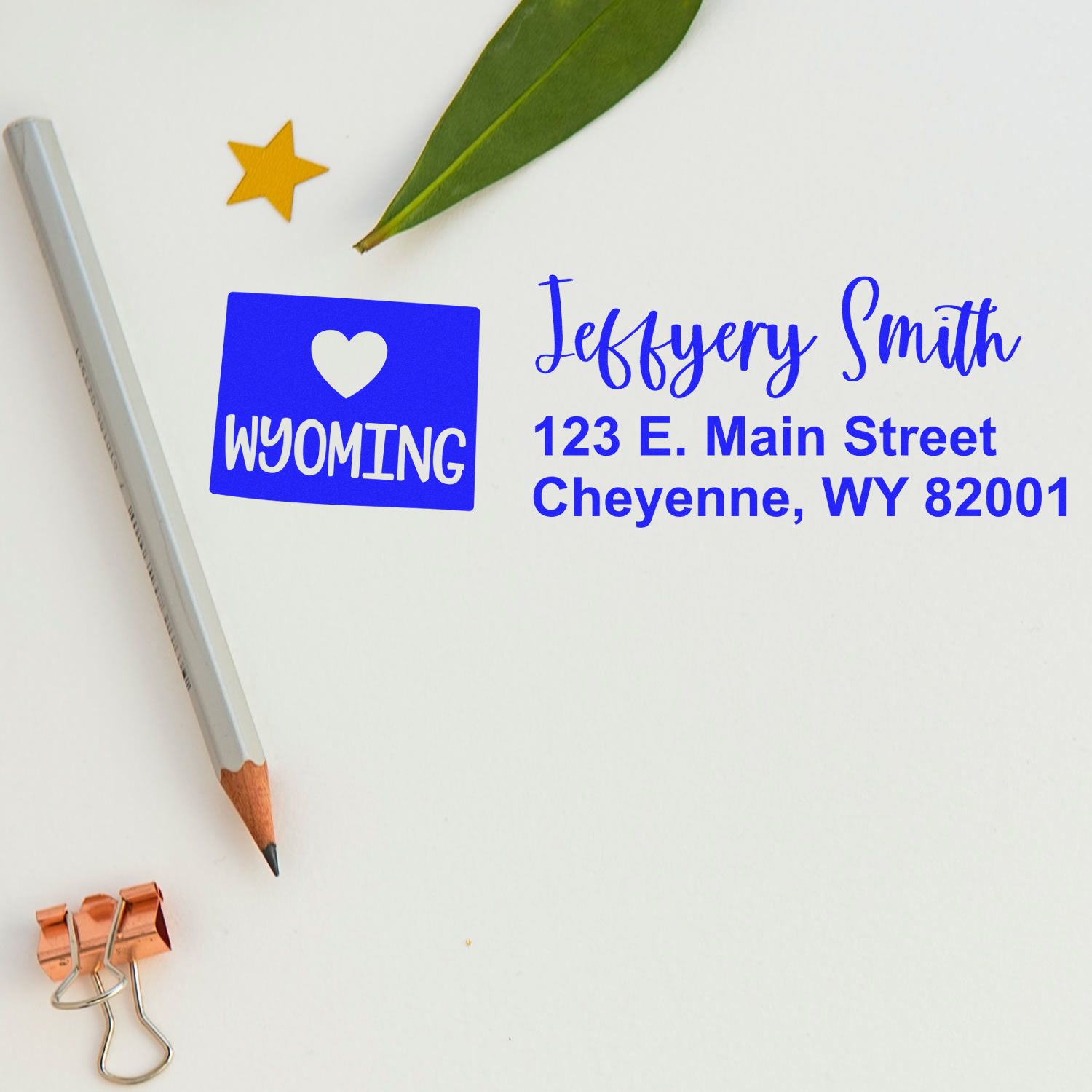 Wyoming State Love Personalized Address Stamp on paper with a pencil, leaf, star sticker, and copper clip. Displays Jeffery Smith, 123 E. Main Street, Cheyenne, WY 82001 in blue text.