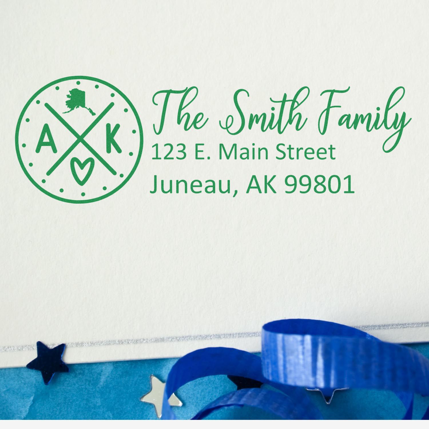 Alaska State Pride Customized Address Stamp featuring a green design with The Smith Family and an Alaska motif, displayed on an envelope with blue ribbon and star decorations.