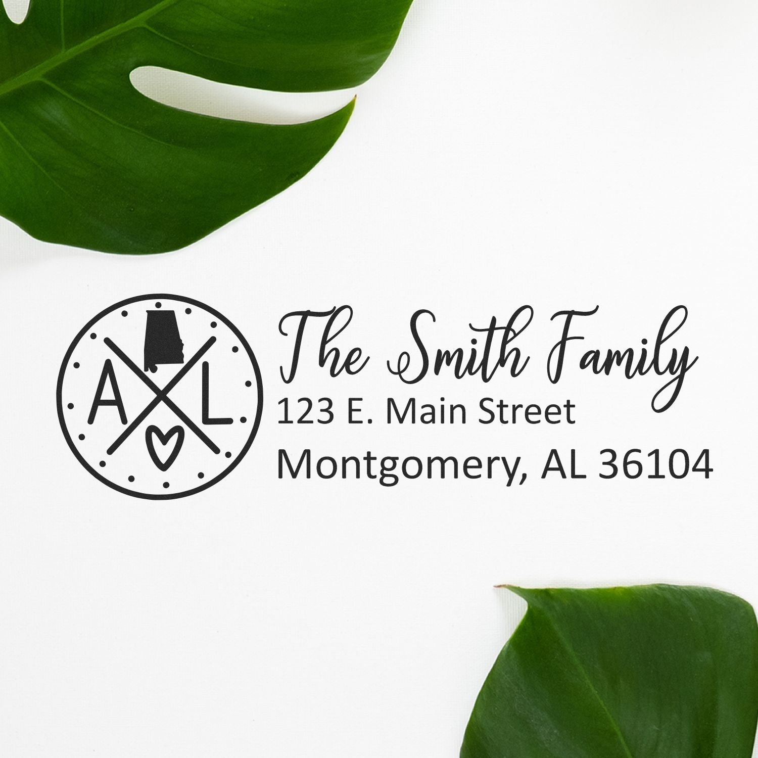 Slim Alabama Customized Pre-Inked Address Stamp displaying 'The Smith Family, 123 E. Main Street, Montgomery, AL 36104' on white background with green leaves.