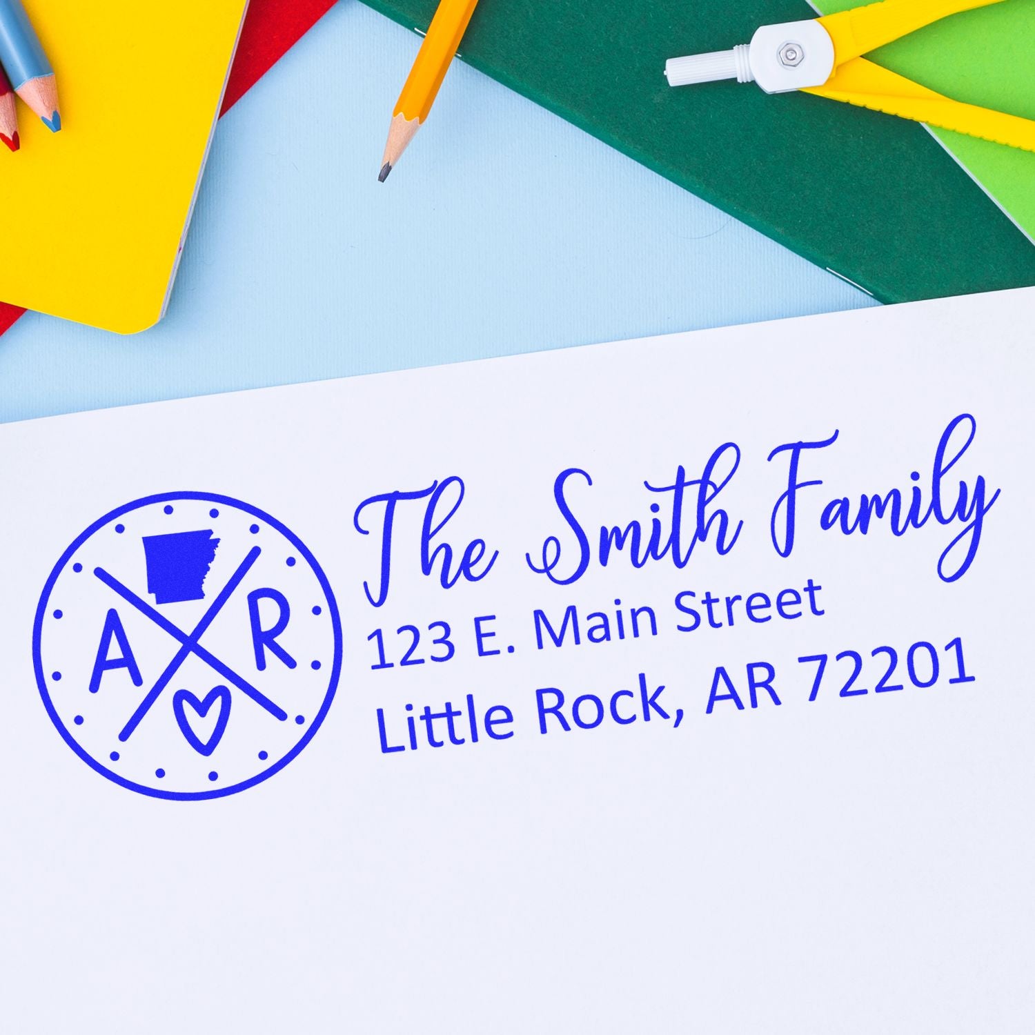 PSI Pre-Inked Arkansas State Pride Customized Address Stamp on white paper with colorful stationery in the background, featuring a blue design with AR and a heart symbol.