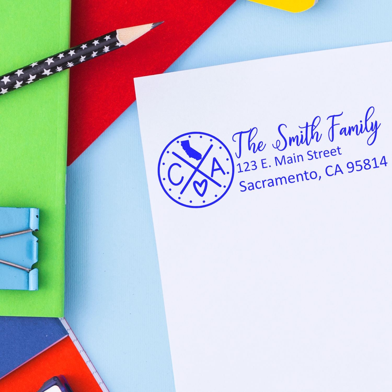 California State Pride Customized Address Stamp on an envelope with colorful stationery. Features a blue design with a heart and state outline, personalized with The Smith Family and address.