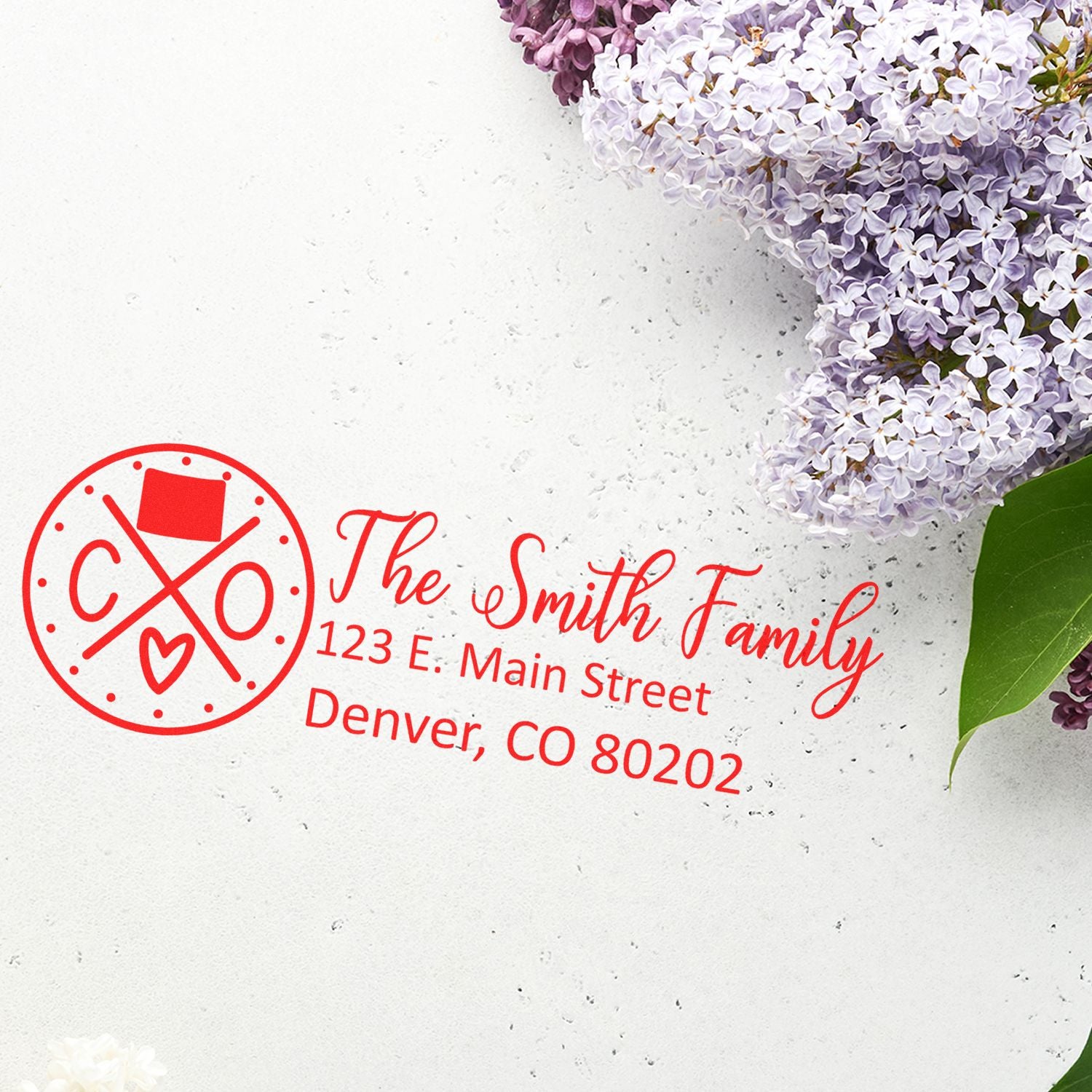 Colorado State Pride Customized Address Stamp in red ink on white paper, featuring a family name and address. Surrounded by lilac flowers and green leaves, showcasing elegant and personalized design.