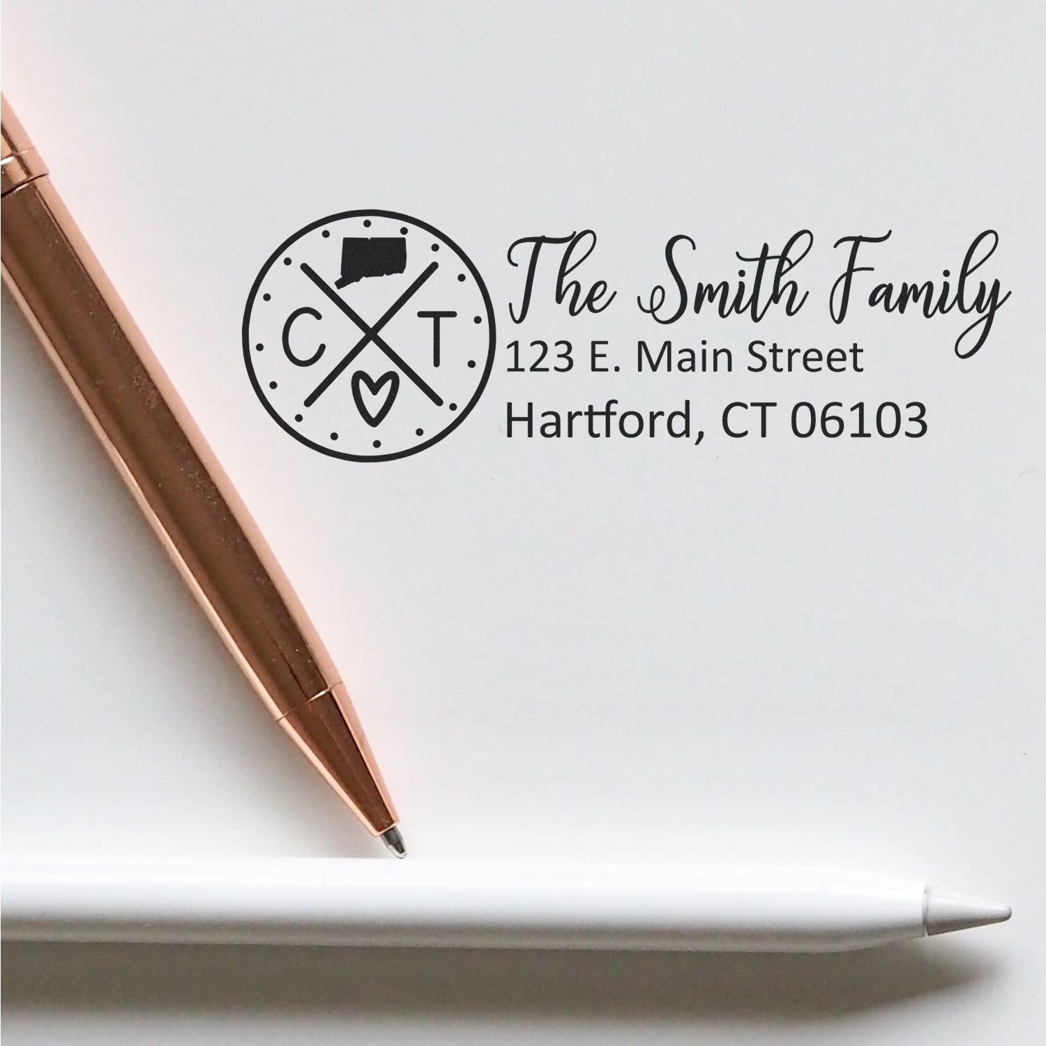 Slim Connecticut Customized Pre-Inked Address Stamp on white paper, featuring a circular design with CT and a heart, next to a rose gold pen and a white stylus.