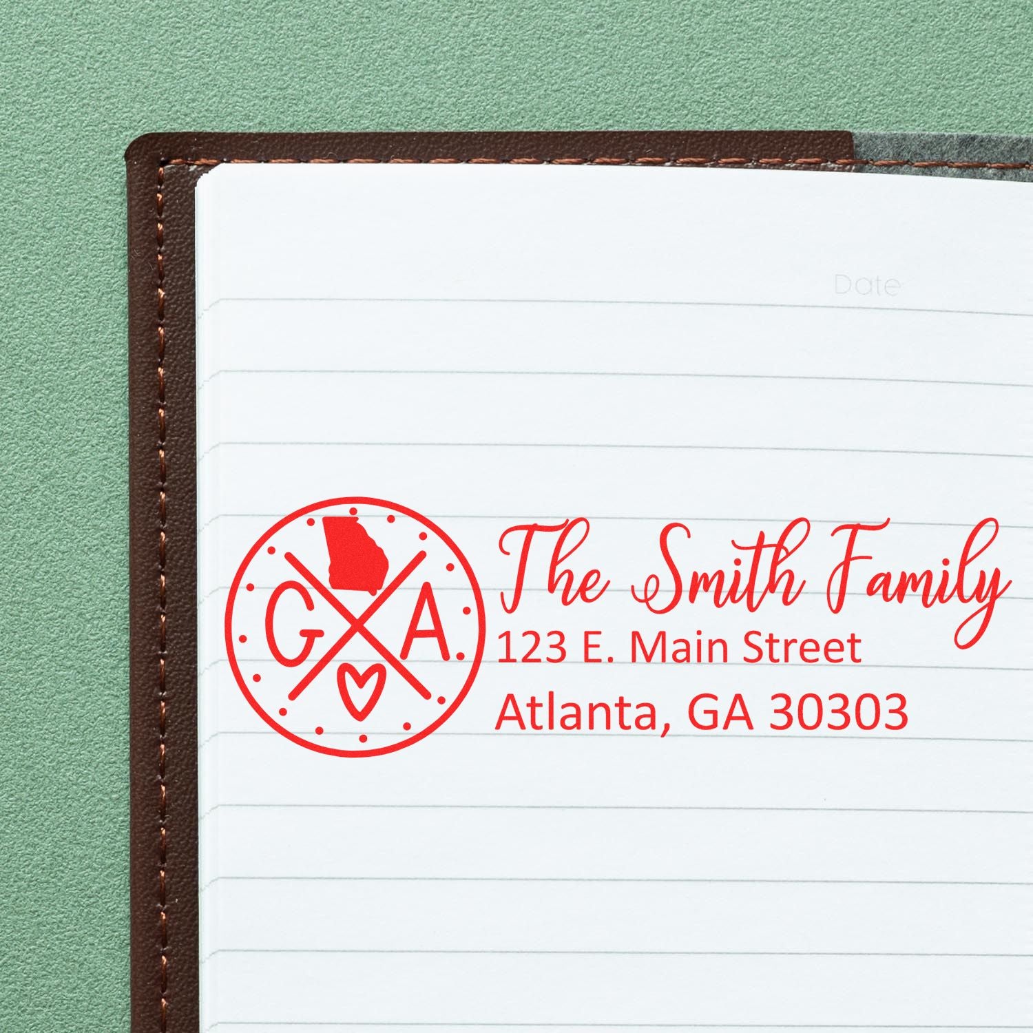 Georgia State Pride Customized Address Stamp in red ink on a notebook page, featuring a circular design with GA and a heart, alongside the address 123 E. Main Street, Atlanta, GA 30303.