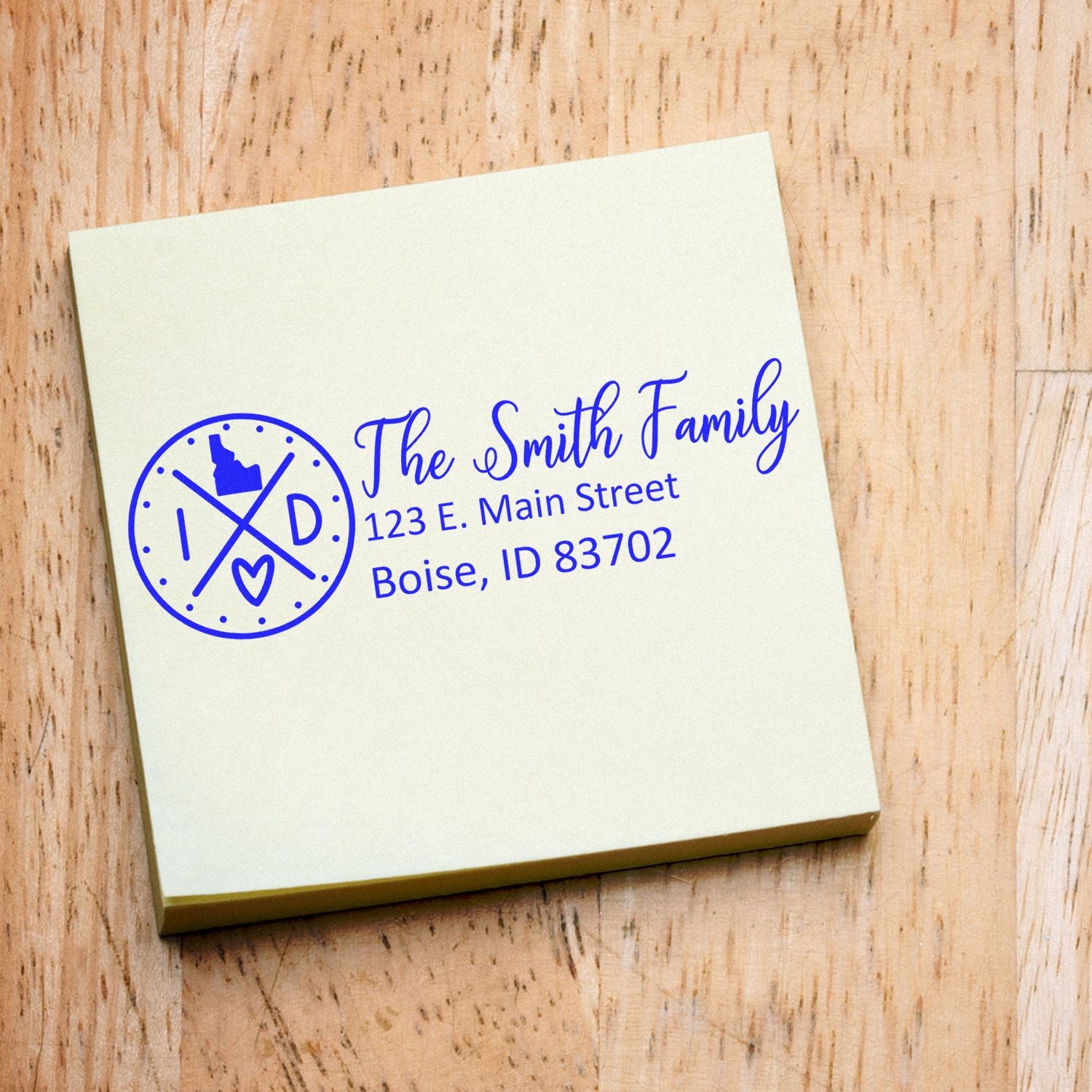 Self-Inking State Love of Idaho Custom Address Stamp on a beige notepad, displaying The Smith Family, 123 E. Main Street, Boise, ID 83702 in blue ink with an Idaho state outline and heart design.