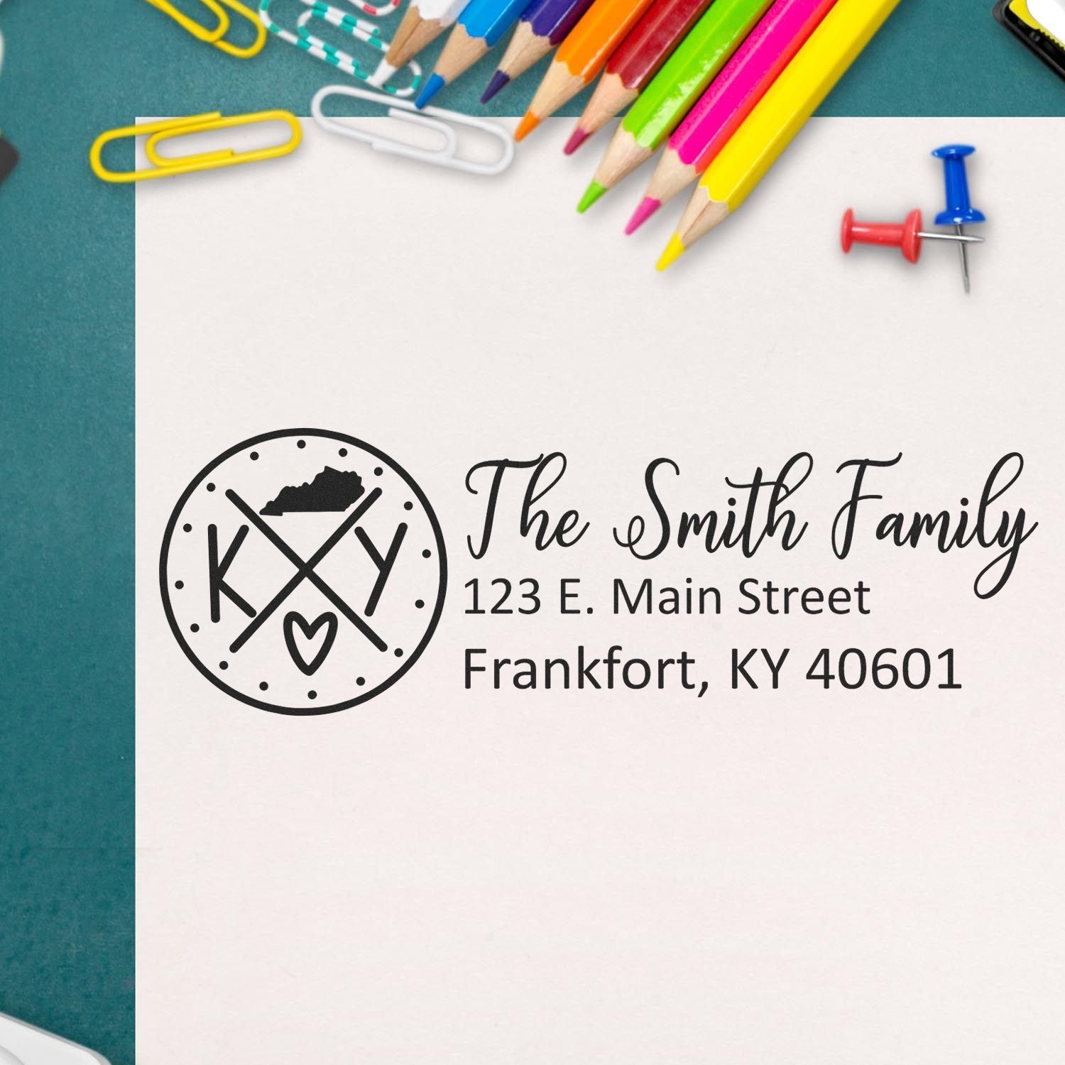 Kentucky State Pride Customized Address Stamp on paper with colorful pencils, paperclips, and a pushpin. The stamp features a Kentucky map and personalized address for the Smith family in Frankfort, KY.