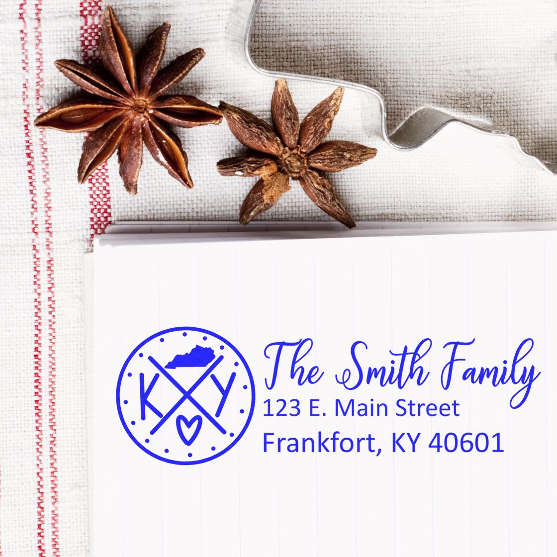 A Self-Inking State Love of Kentucky Custom Address Stamp on a notepad with a Kentucky design, surrounded by star anise and a cookie cutter on a textured cloth.