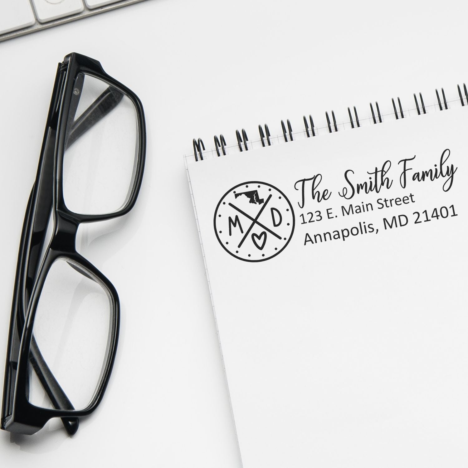 Notebook with The Smith Family and address stamped using the Maryland State Pride Customized Address Stamp. Glasses and keyboard nearby.