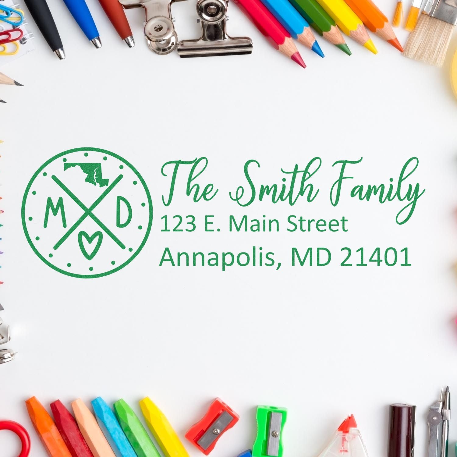 A Slim Maryland Customized Pre-Inked Address Stamp on paper, surrounded by colorful stationery, displaying The Smith Family, 123 E. Main Street, Annapolis, MD 21401 in green ink.