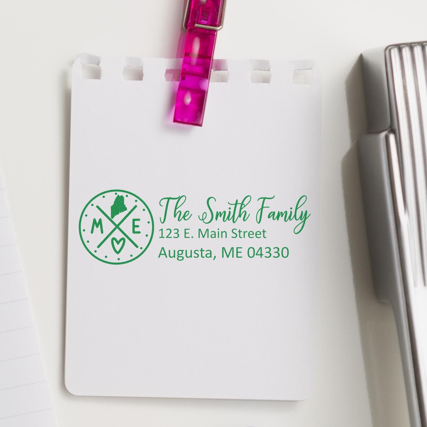 PSI Pre-Inked Maine State Pride Customized Address Stamp on a notepad, displaying The Smith Family, 123 E. Main Street, Augusta, ME 04330 in green ink with a Maine state outline and heart design.