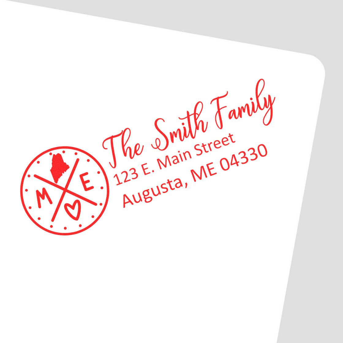 Red Maine State Pride Customized Address Stamp on a white envelope, featuring a circular design with ME and a heart, personalized with The Smith Family, 123 E. Main Street, Augusta, ME 04330.