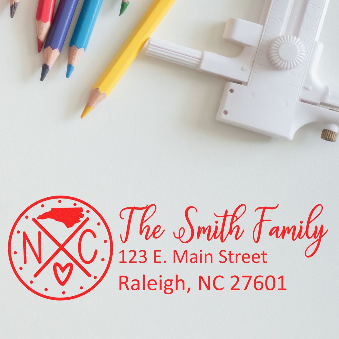 PSI Pre-Inked North Carolina State Pride Customized Address Stamp featuring a red NC design and personalized address for the Smith Family, shown on a white background with colored pencils and a ruler.