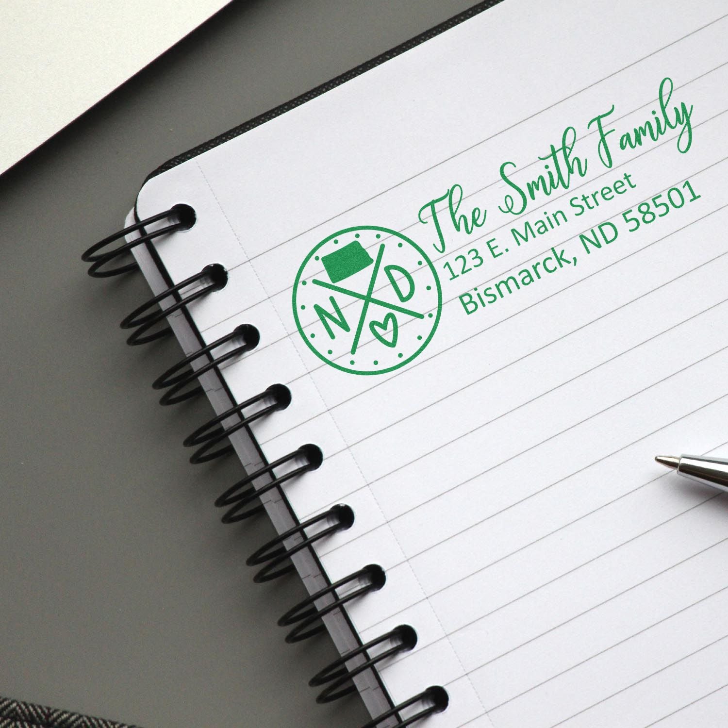 PSI Pre-Inked North Dakota State Pride Customized Address Stamp on a notebook page, displaying The Smith Family with an address in green ink, alongside a pen.