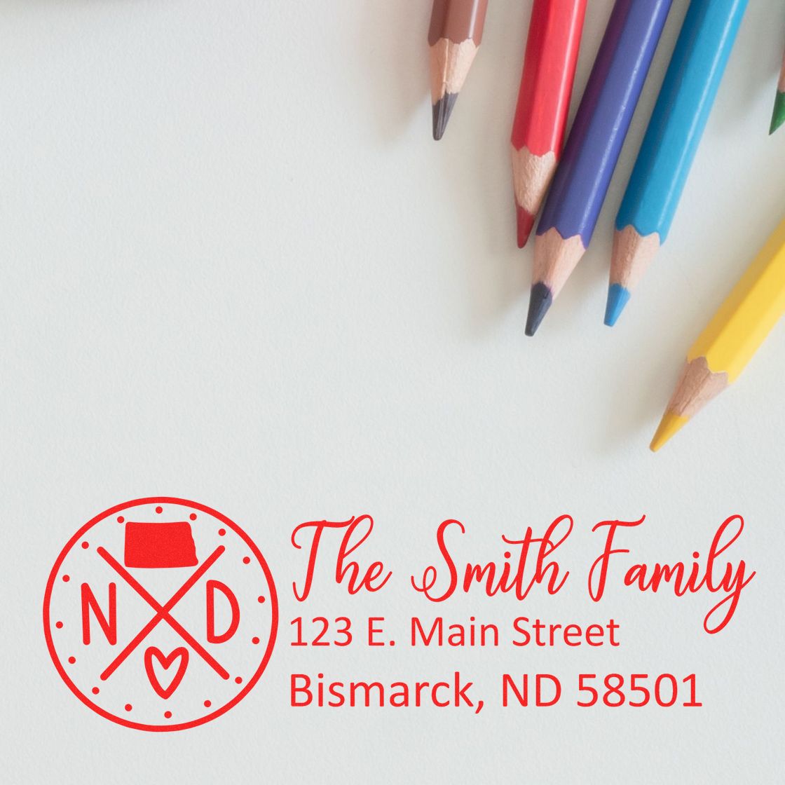 Slim North Dakota Customized Pre-Inked Address Stamp in red ink on white paper, featuring The Smith Family and address, with colored pencils nearby.