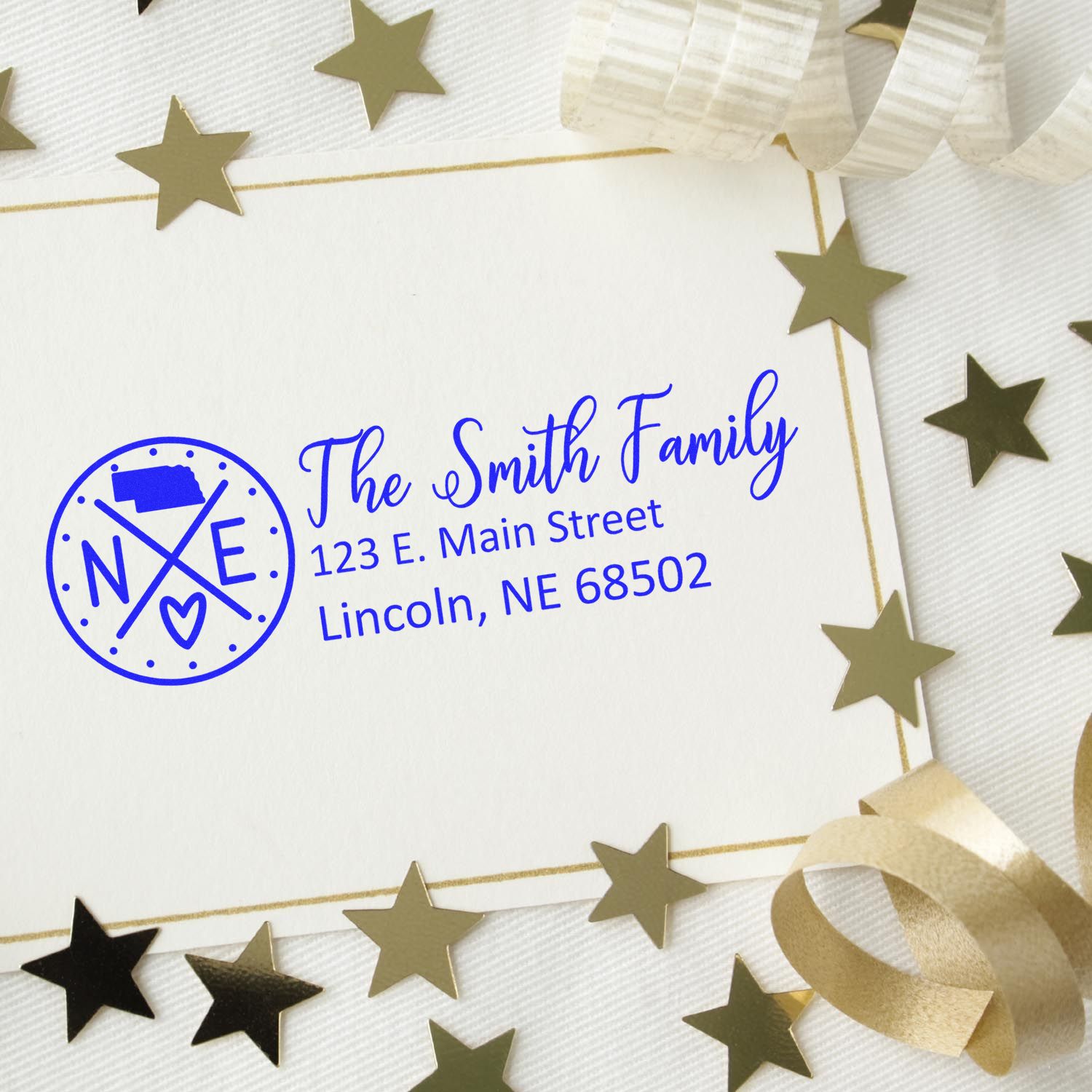 Self-Inking State Love of Nebraska Custom Address Stamp on an envelope with gold stars and ribbon, featuring a Nebraska state design and personalized address for the Smith Family in blue ink.