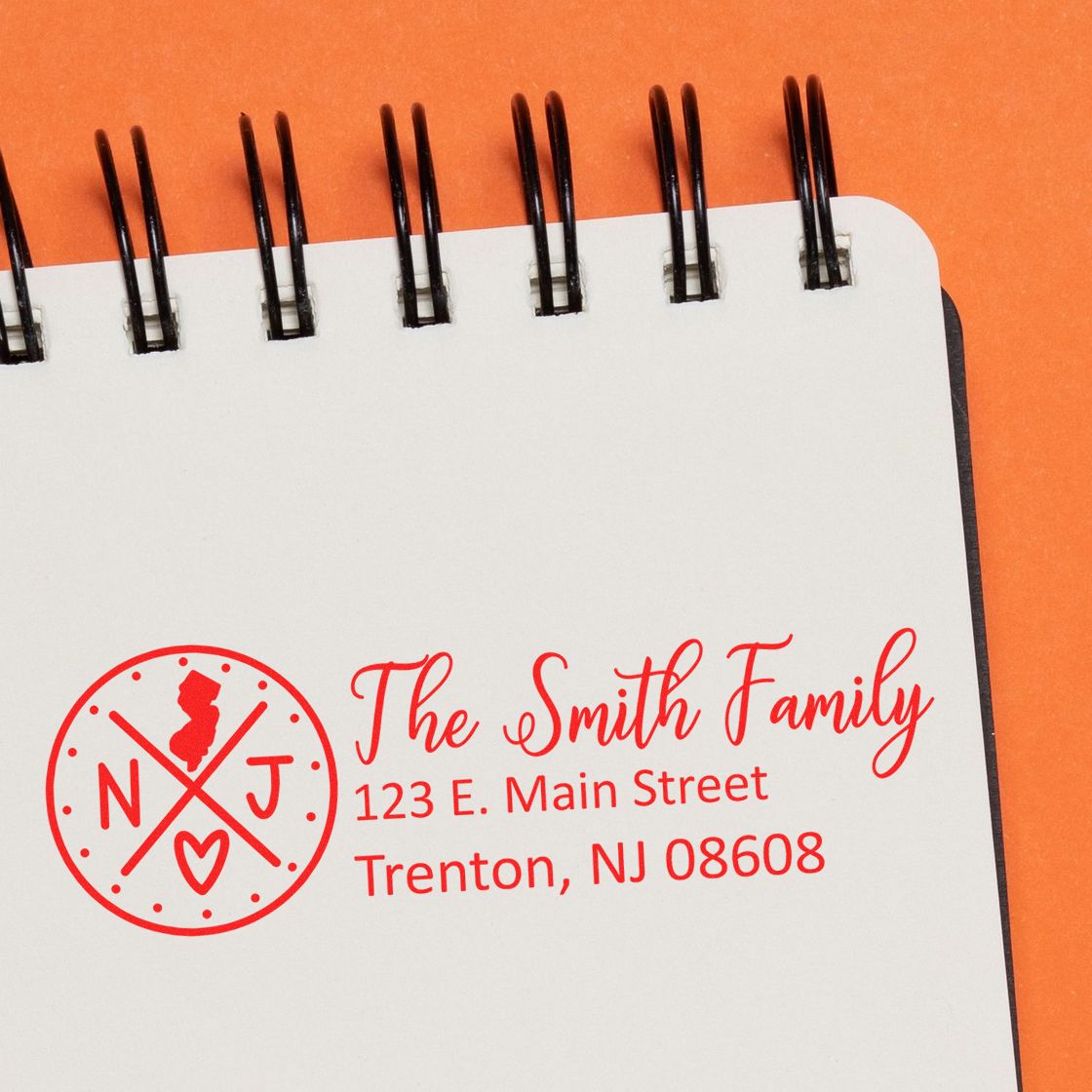 Slim New Jersey Customized Pre-Inked Address Stamp on a notepad, displaying The Smith Family, 123 E. Main Street, Trenton, NJ 08608 in red ink with a circular NJ logo.