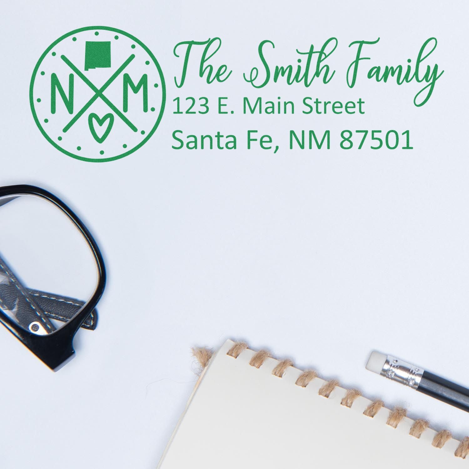 New Mexico State Pride Customized Address Stamp featuring a green design with NM and a heart, shown on an envelope with glasses and a notebook nearby.