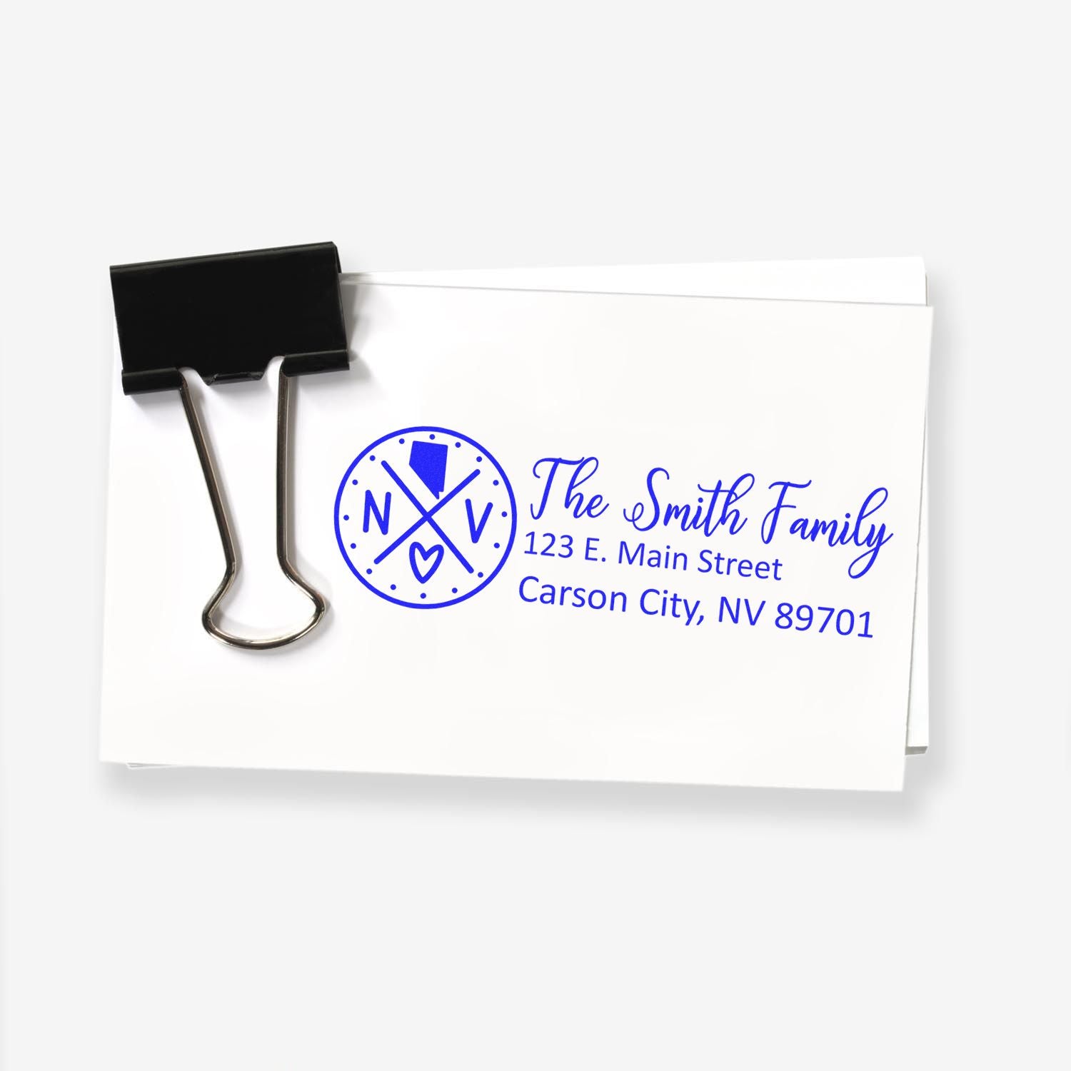 Slim Nevada Customized Pre-Inked Address Stamp on white envelope with blue ink, featuring a circular design and text for The Smith Family, 123 E. Main Street, Carson City, NV 89701, clipped together.