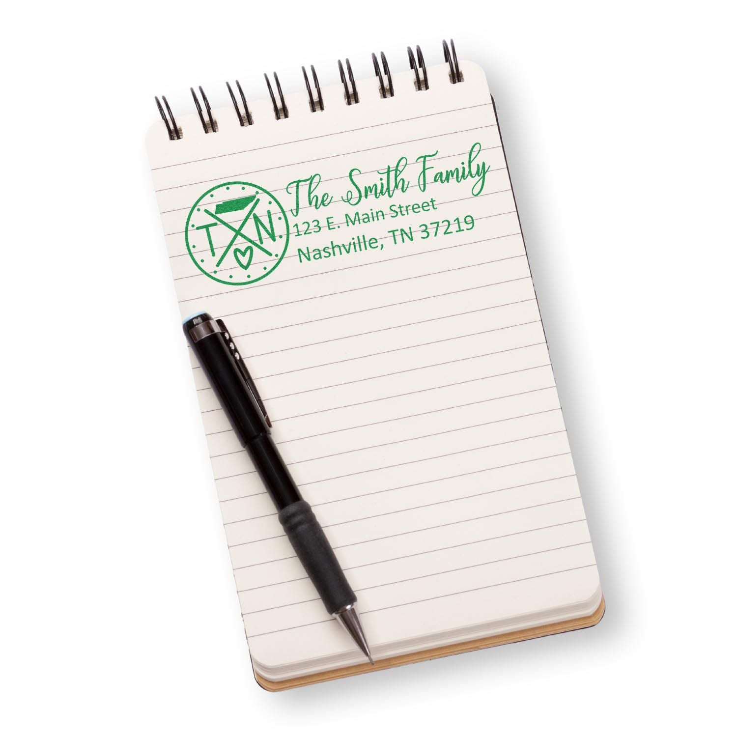 A Slim Tennessee Customized Pre-Inked Address Stamp imprints a green address on a spiral notebook page, accompanied by a black pen.