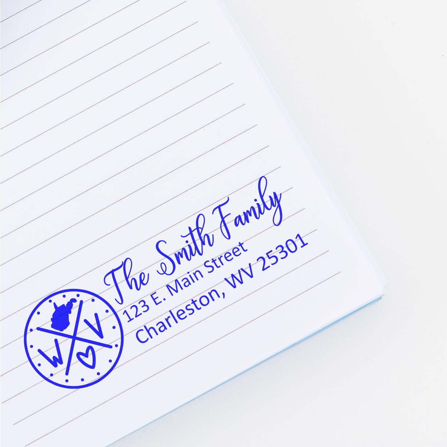 PSI Pre-Inked West Virginia State Pride Customized Address Stamp on a lined notebook, displaying The Smith Family, 123 E. Main Street, Charleston, WV 25301 in blue ink.