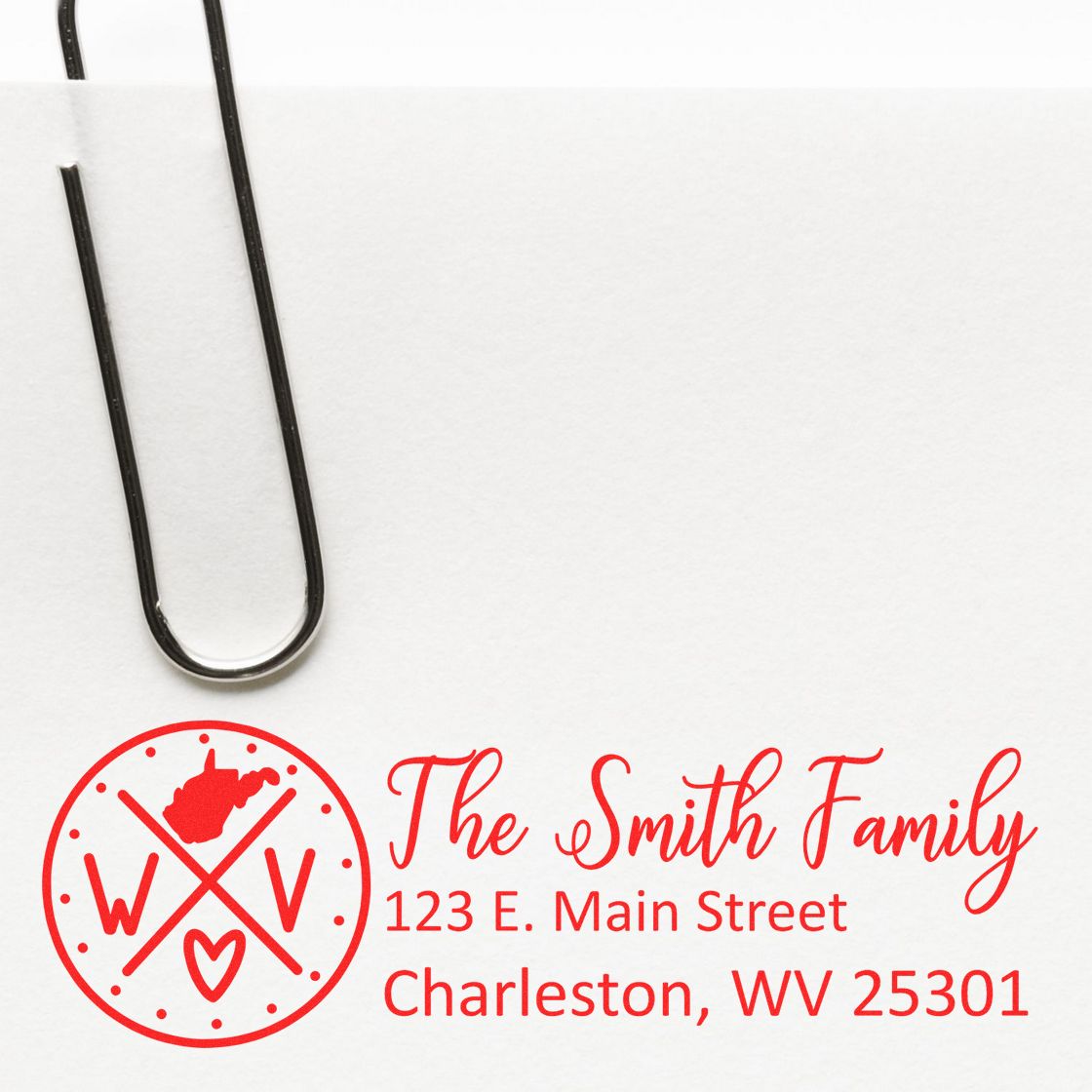 Self-Inking State Love of West Virginia Custom Address Stamp on white paper, featuring a red design with The Smith Family and an address in Charleston, WV, next to a paperclip.