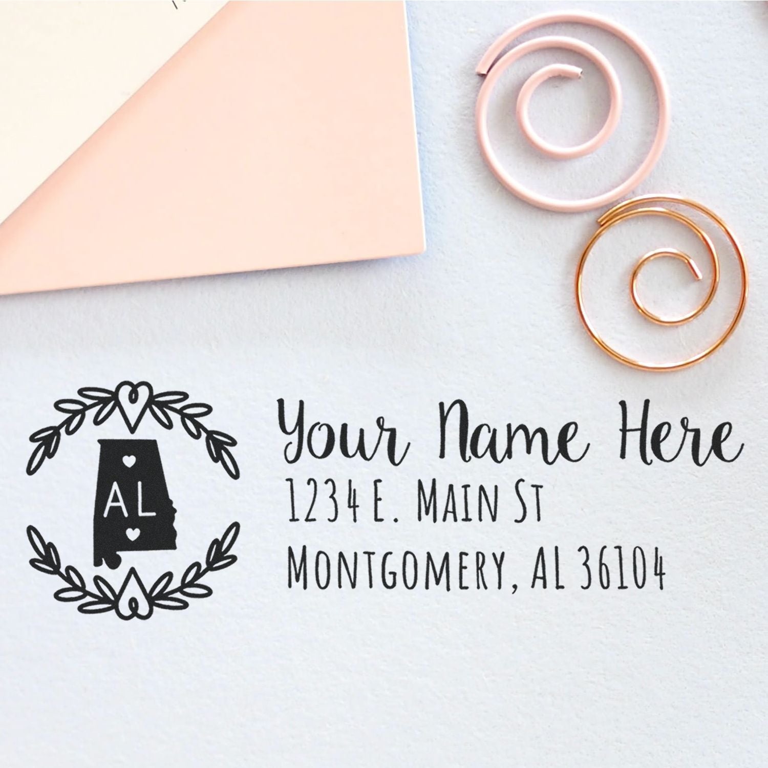 Alabama State Custom Return Address Stamp on a light surface with decorative spirals, featuring a state outline and floral design, personalized with name and address in elegant script.