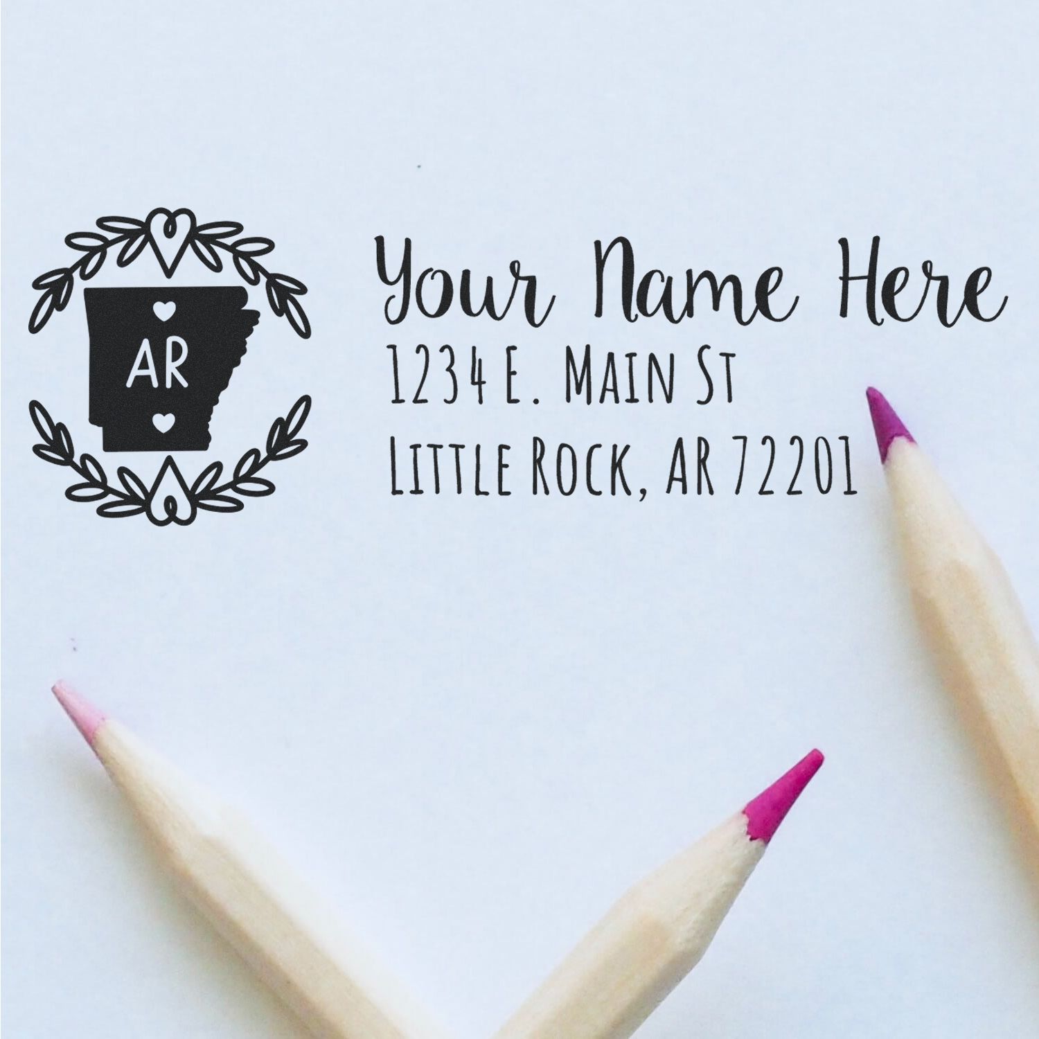 Arkansas State Custom Return Address Stamp on white paper with a decorative state outline and text. Two pencils with pink tips are placed nearby.