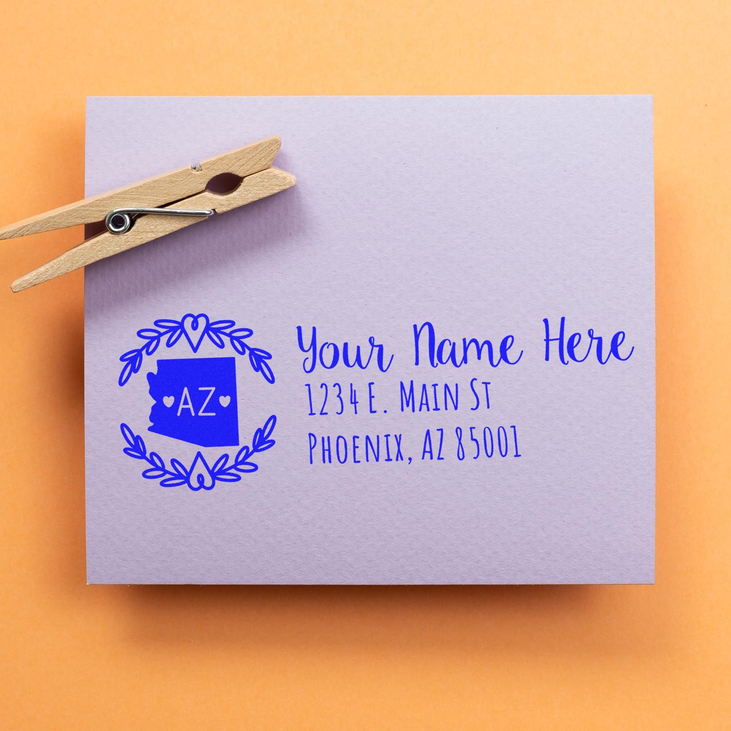 Self-Inking State Wreath of Arizona Address Stamp on a lavender envelope with a wooden clothespin, featuring a blue Arizona state design and sample address text.