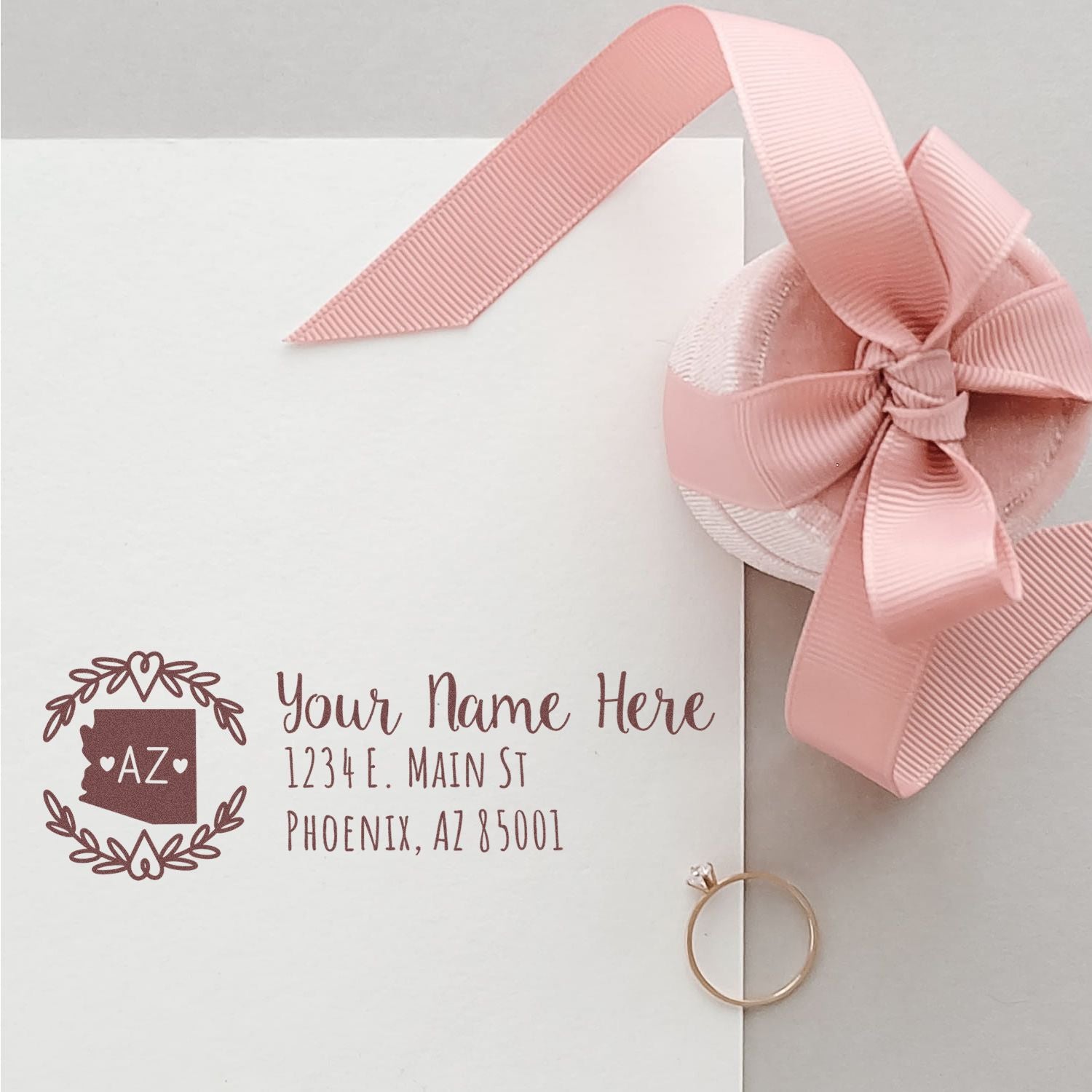 Arizona State Custom Return Address Stamp on an envelope with a pink ribbon and ring. The stamp features a decorative border and placeholder text for name and address in Phoenix, AZ.