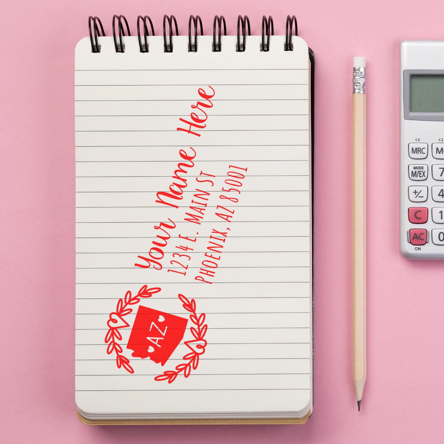 Self-Inking State Wreath of Arizona Address Stamp on a notepad with a red design, next to a pencil and calculator on a pink background.