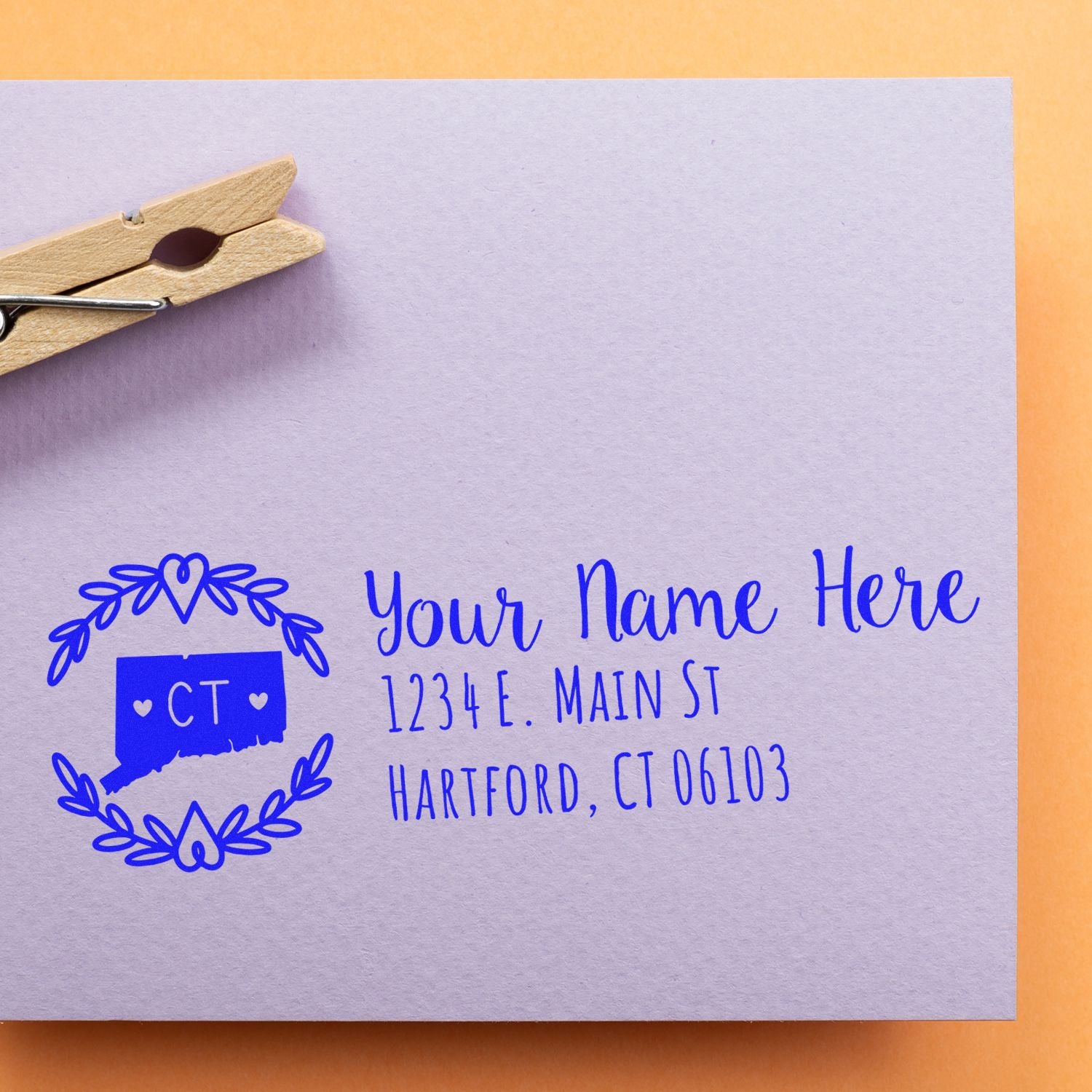 Connecticut State Custom Return Address Stamp on a lavender envelope with a blue design featuring the state outline and address details. A wooden clothespin is clipped to the envelope on an orange background.