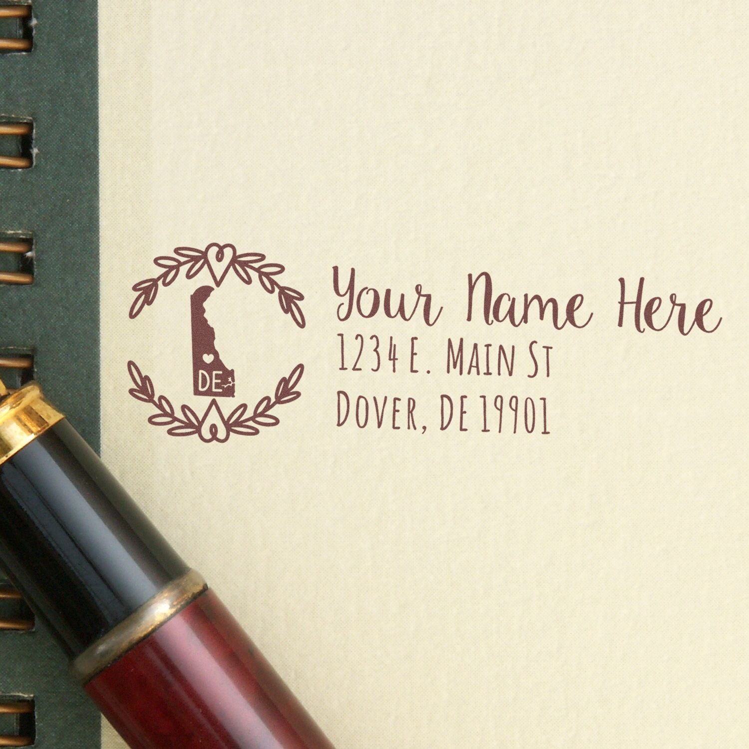 Delaware State Custom Return Address Stamp on beige paper next to a pen. Features a decorative border with a Delaware state outline, customizable name, and address fields.