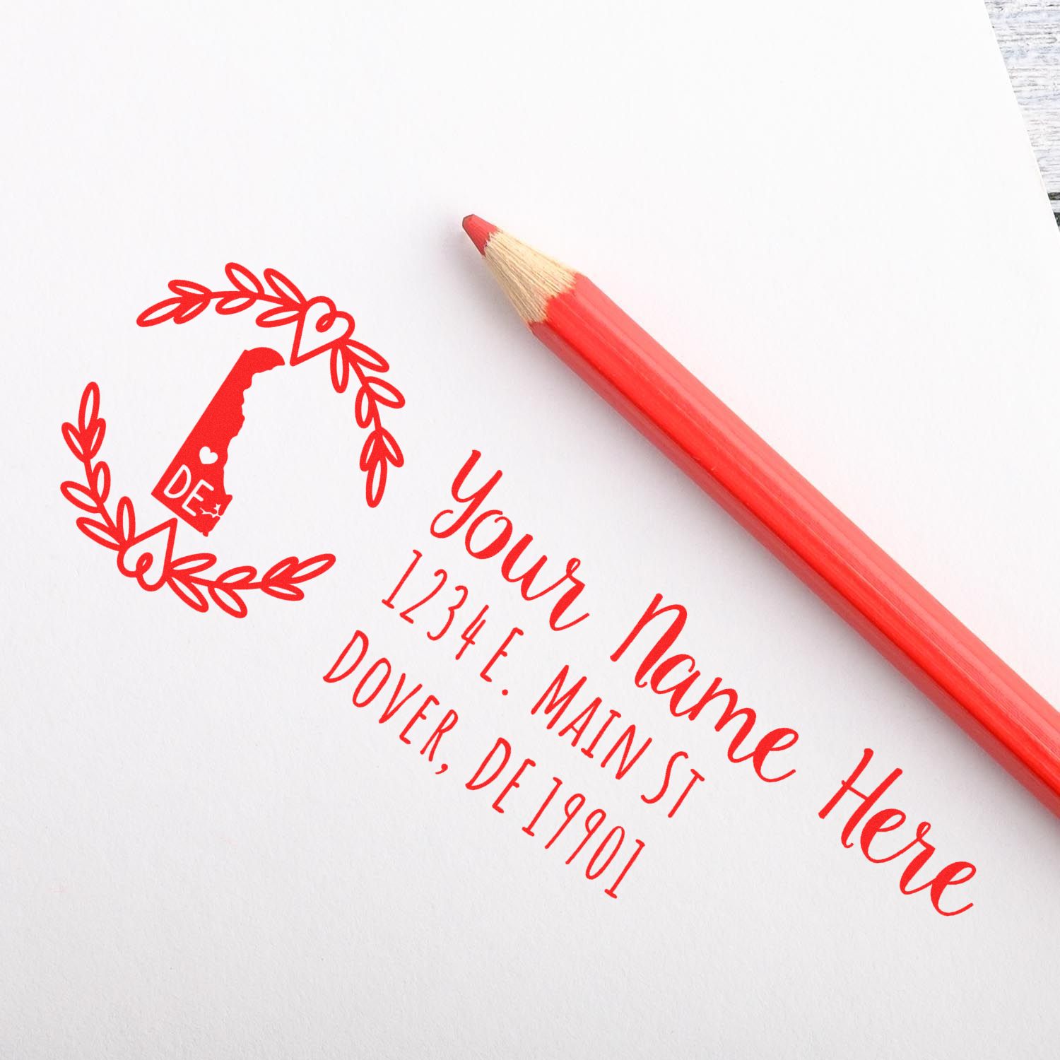 Image of a Delaware State Custom Return Address Stamp on paper with a red pencil. The stamp features a Delaware outline and decorative border, displaying a sample address in elegant red script.