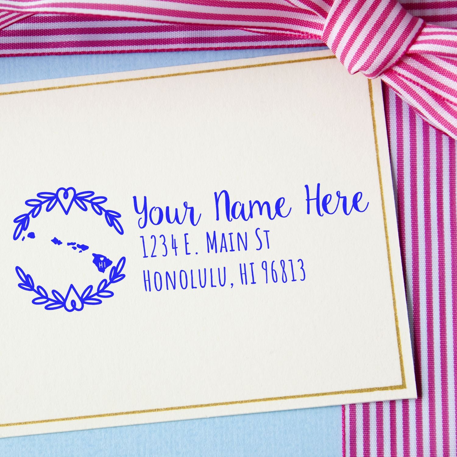 Self-Inking State Wreath of Hawaii Address Stamp on a card with a pink striped ribbon, featuring a blue wreath design and sample address text in elegant font.