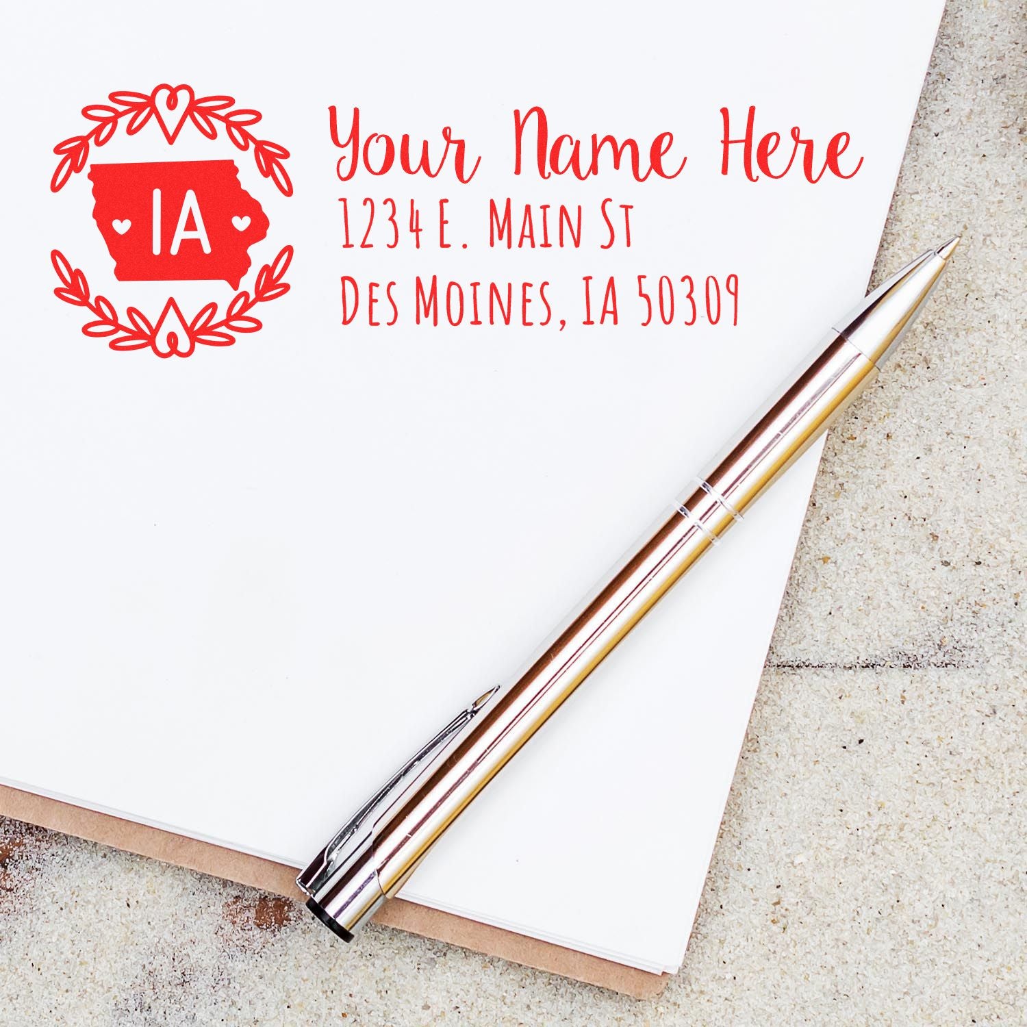 Iowa State Custom Return Address Stamp on white paper with a red design, featuring a pen nearby. Text includes a sample address in Des Moines, IA.