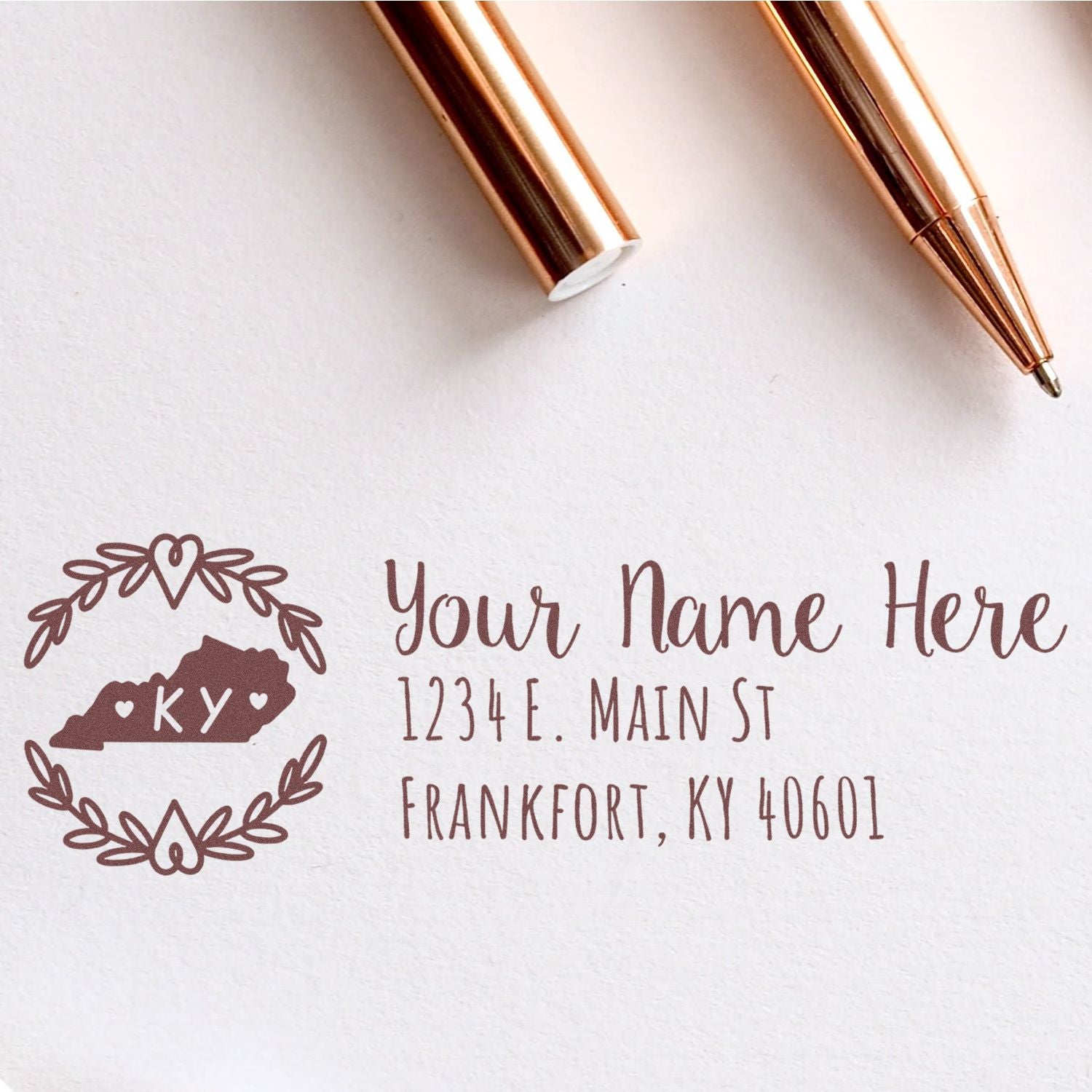 Kentucky State Custom Return Address Stamp featuring a decorative KY state outline with hearts, personalized name, and address in elegant script. Shown with rose gold pens on white paper.