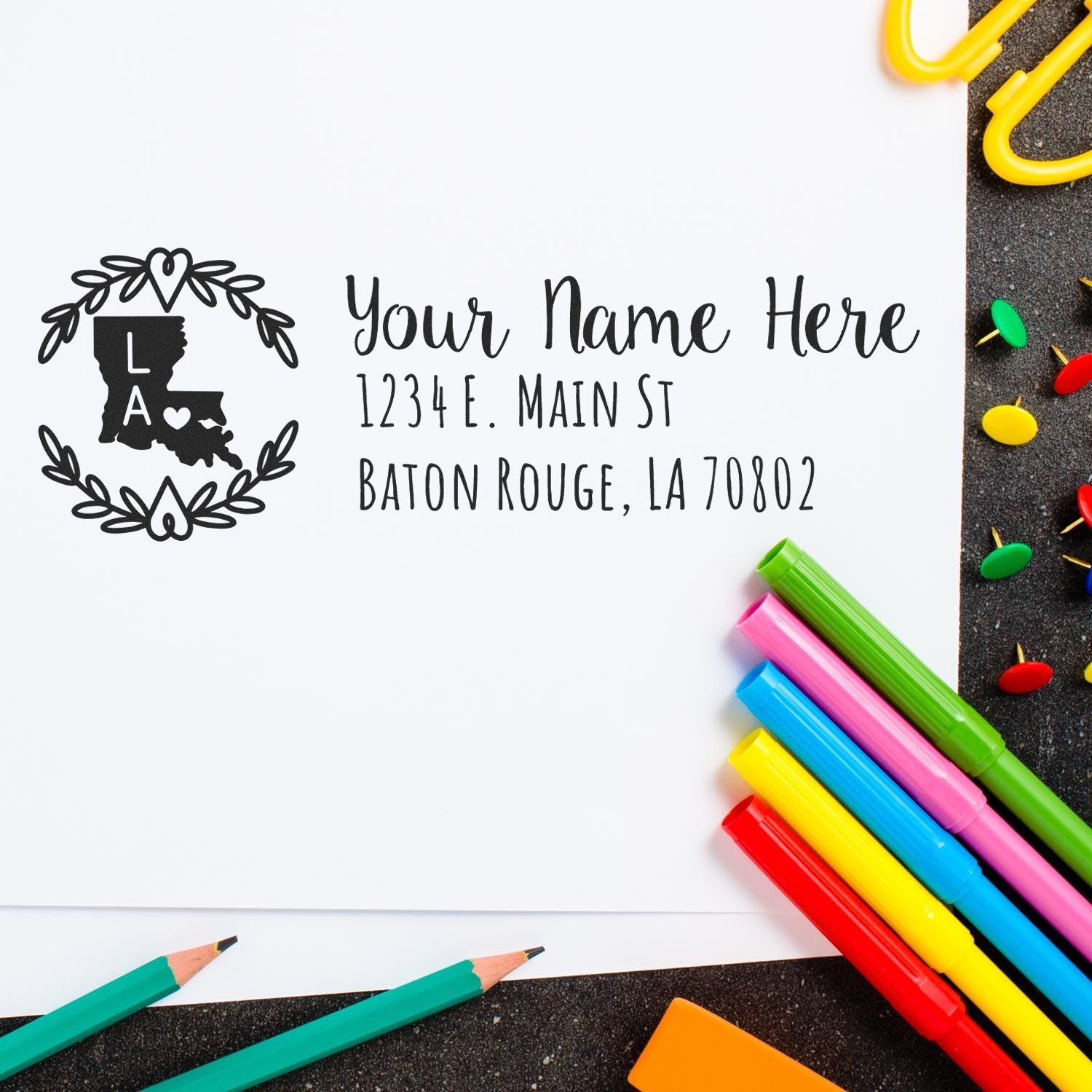 Slim Louisiana Personalized Pre-Inked Address Stamp on white paper, surrounded by colorful pens and push pins, featuring a decorative state outline and customizable address text.