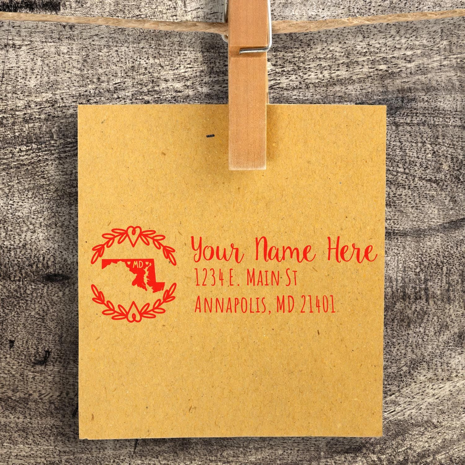 Maryland State Custom Return Address Stamp on brown paper, featuring a red outline of Maryland with decorative elements, clipped to a wooden surface.